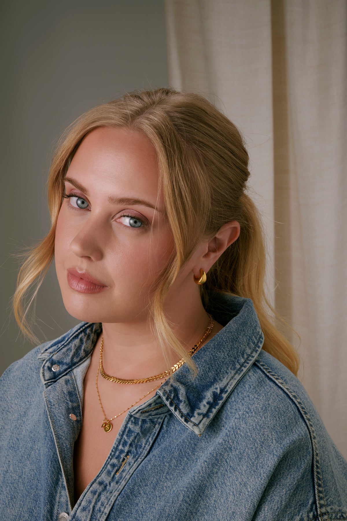 A close-up shot of a model wearing the Bolded Little Sis Earrings in gold, featuring their chunky hoop design. 