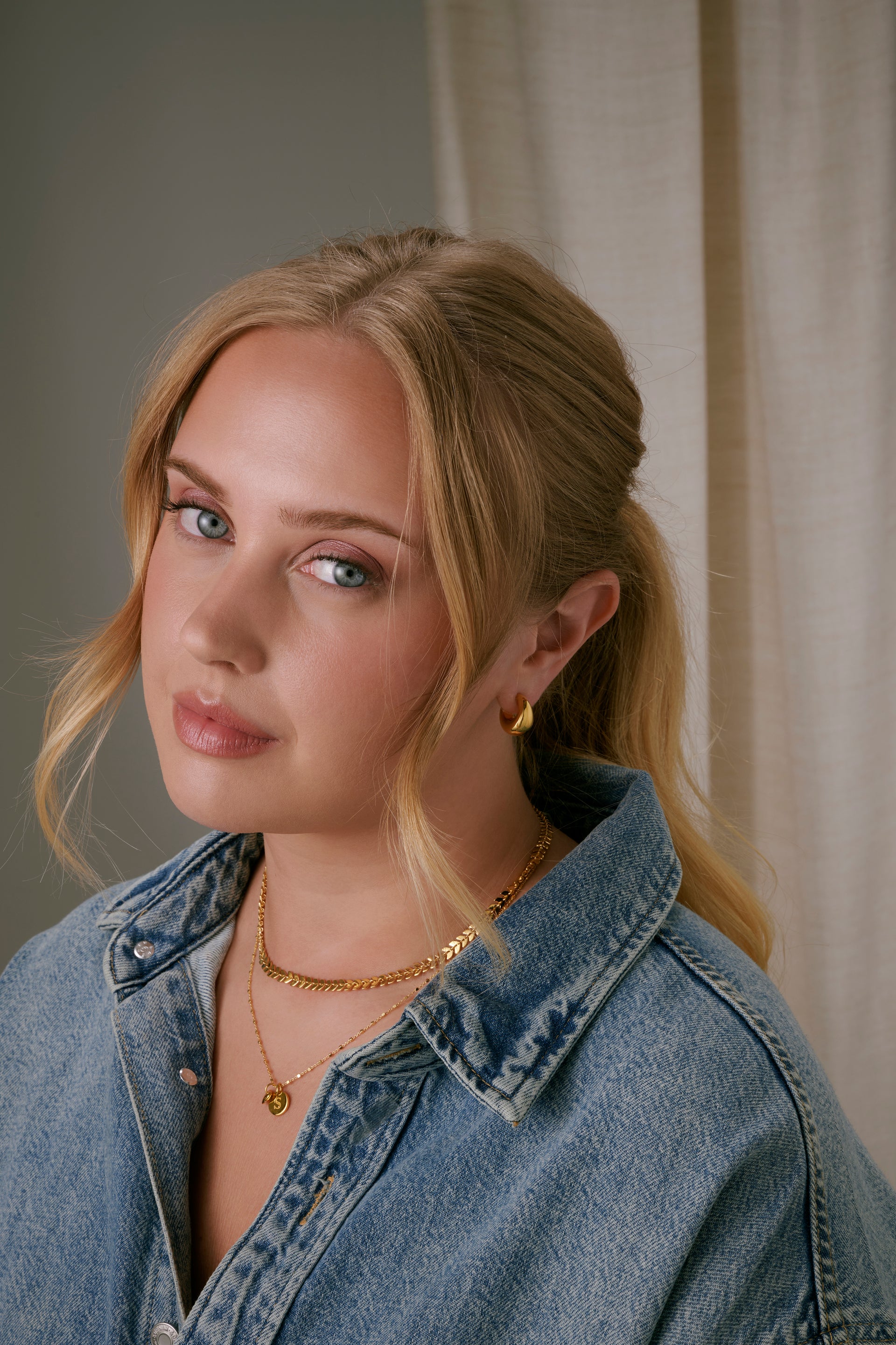 A close-up shot of a model wearing the Bolded Little Sis Earrings in gold, featuring their chunky hoop design. 