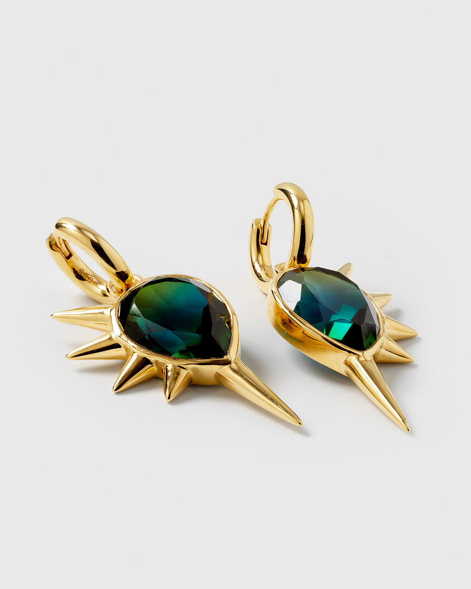 A product shot of the Queen Of Spikes Earrings in gold, featuring a large, teardrop-shaped teal quartz stone surrounded by prominent gold spikes, hanging from a small gold hoop.