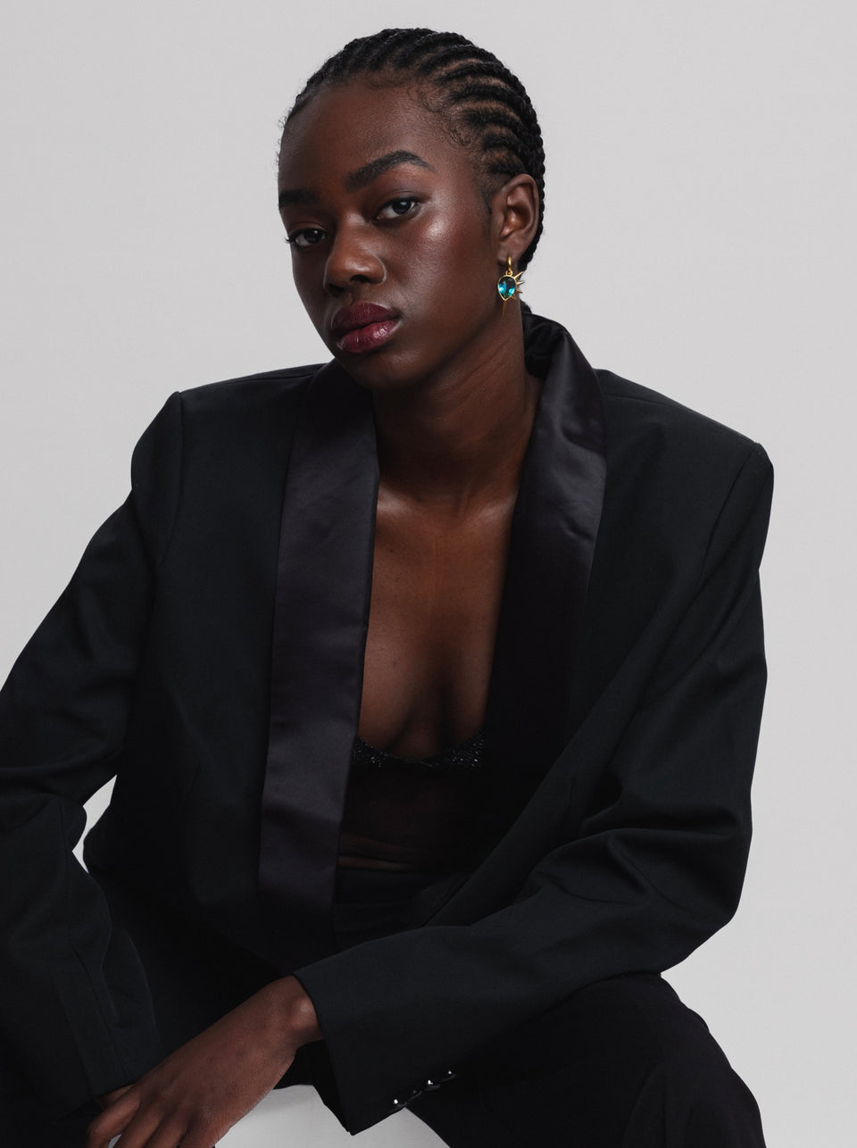 A model wearing the Queen Of Spikes Earrings in gold, featuring a large teal quartz stone with a spiky gold setting.