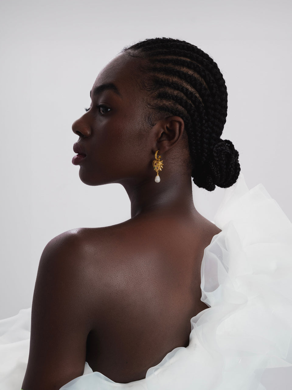 A side profile shot of a model wearing the gold Drama Queen Heart Pearl Earring, featuring a spiky heart charm with set stones and a dangling freshwater pearl.