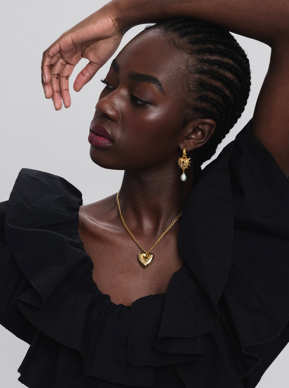 A model shot of the gold Fat Heart Necklace with its chunky chain and pendant, paired with the gold Drama Queen Heart Pearl Earring which features a spiky heart design and a dangling pearl.