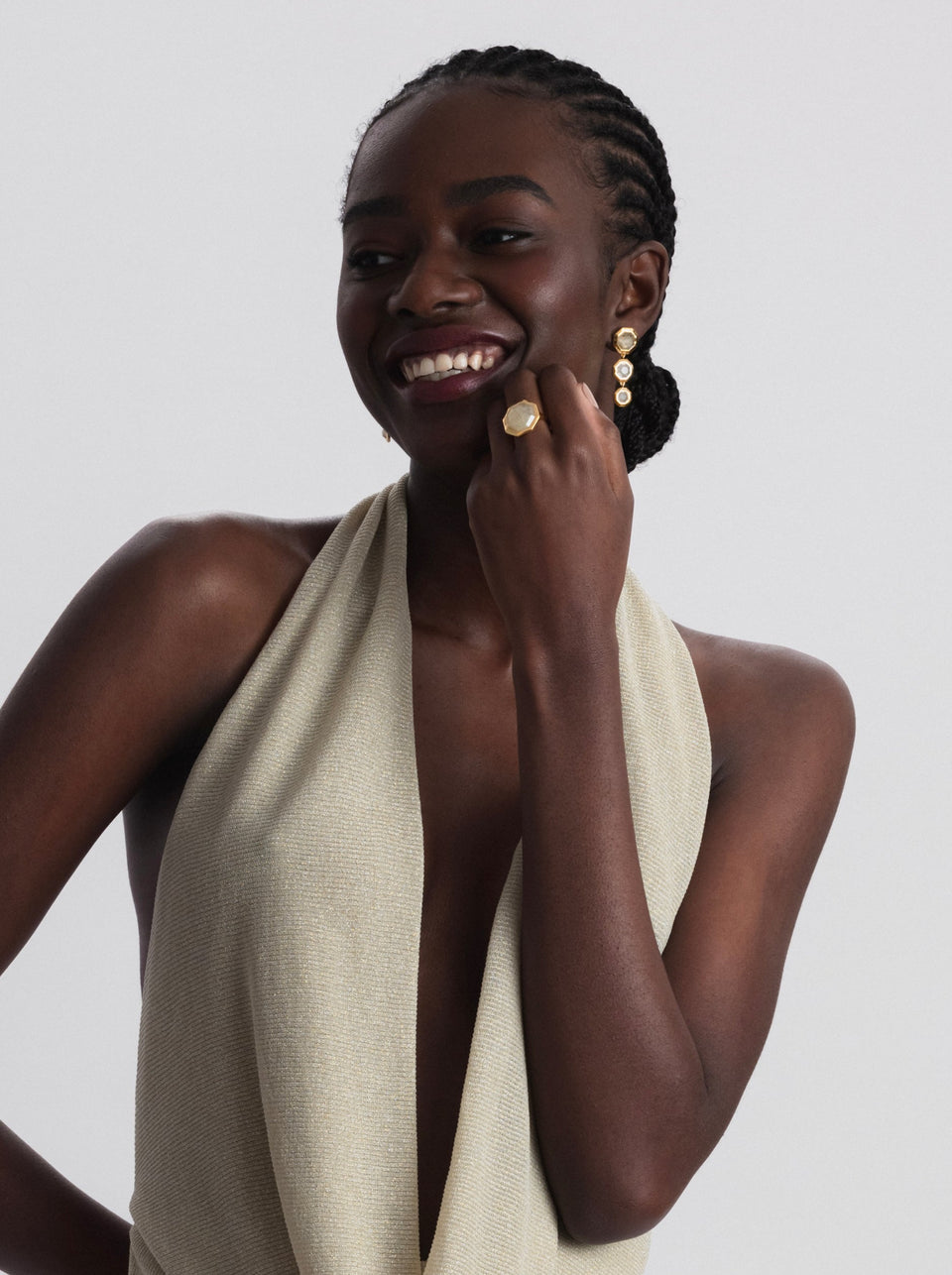 A smiling model wearing the gold Octagon Ring with its large, octagonal golden rutile stone, paired with a set of matching gold drop earrings.