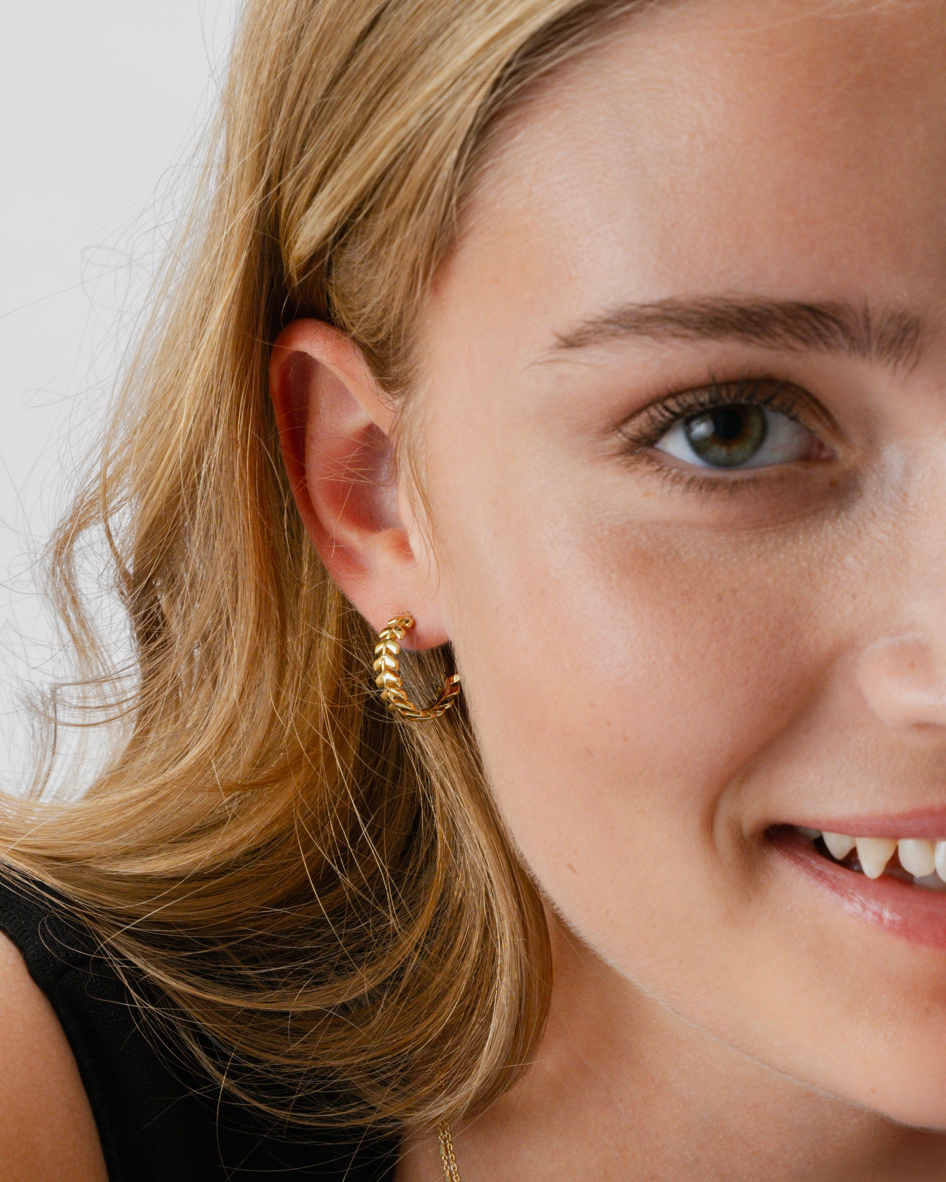A close-up shot of a model wearing the Layers Olivia Hoops in gold, which feature a beautiful pattern of small, leaf-like parts.