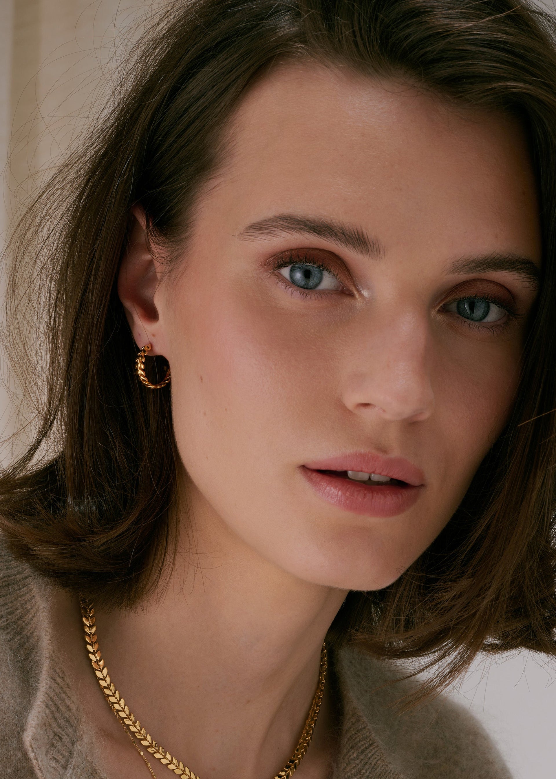 A close-up of gold hoop earrings with a leaf-like pattern, paired with a matching gold necklace.