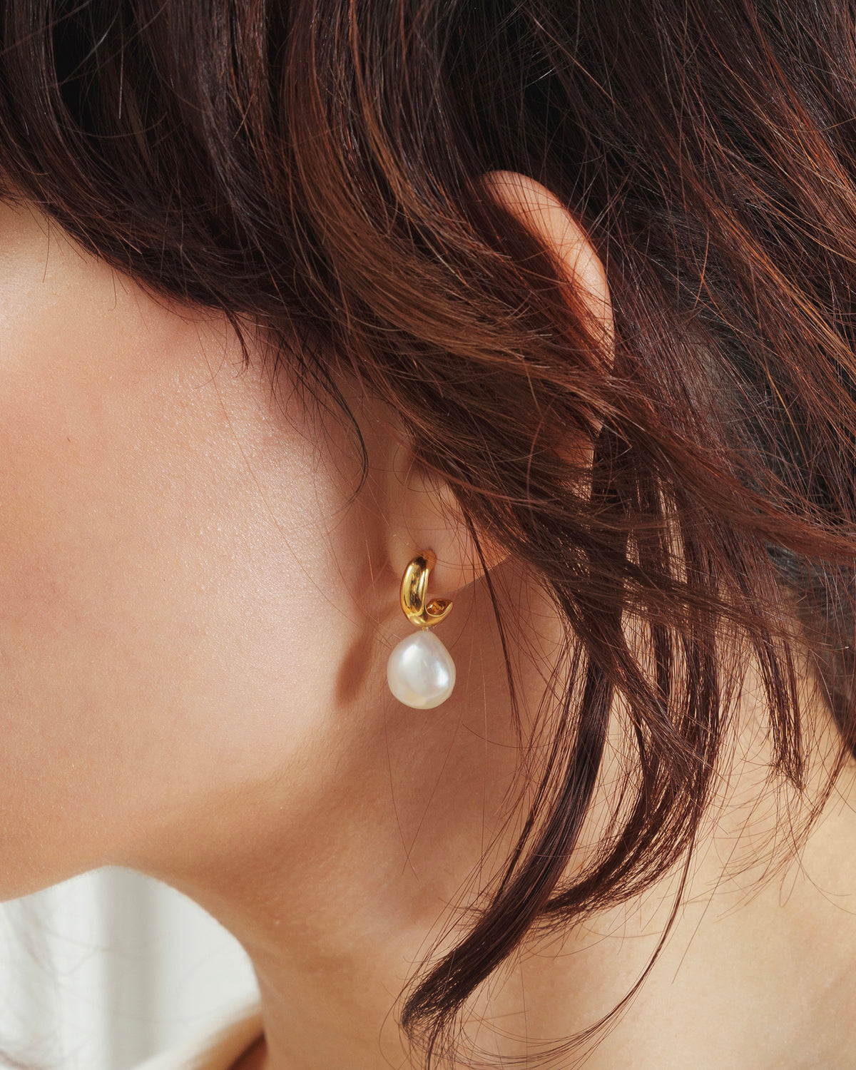 Close-up of a model wearing the Paxton gold earring, featuring a gold earring with a dangling baroque freshwater pearl.