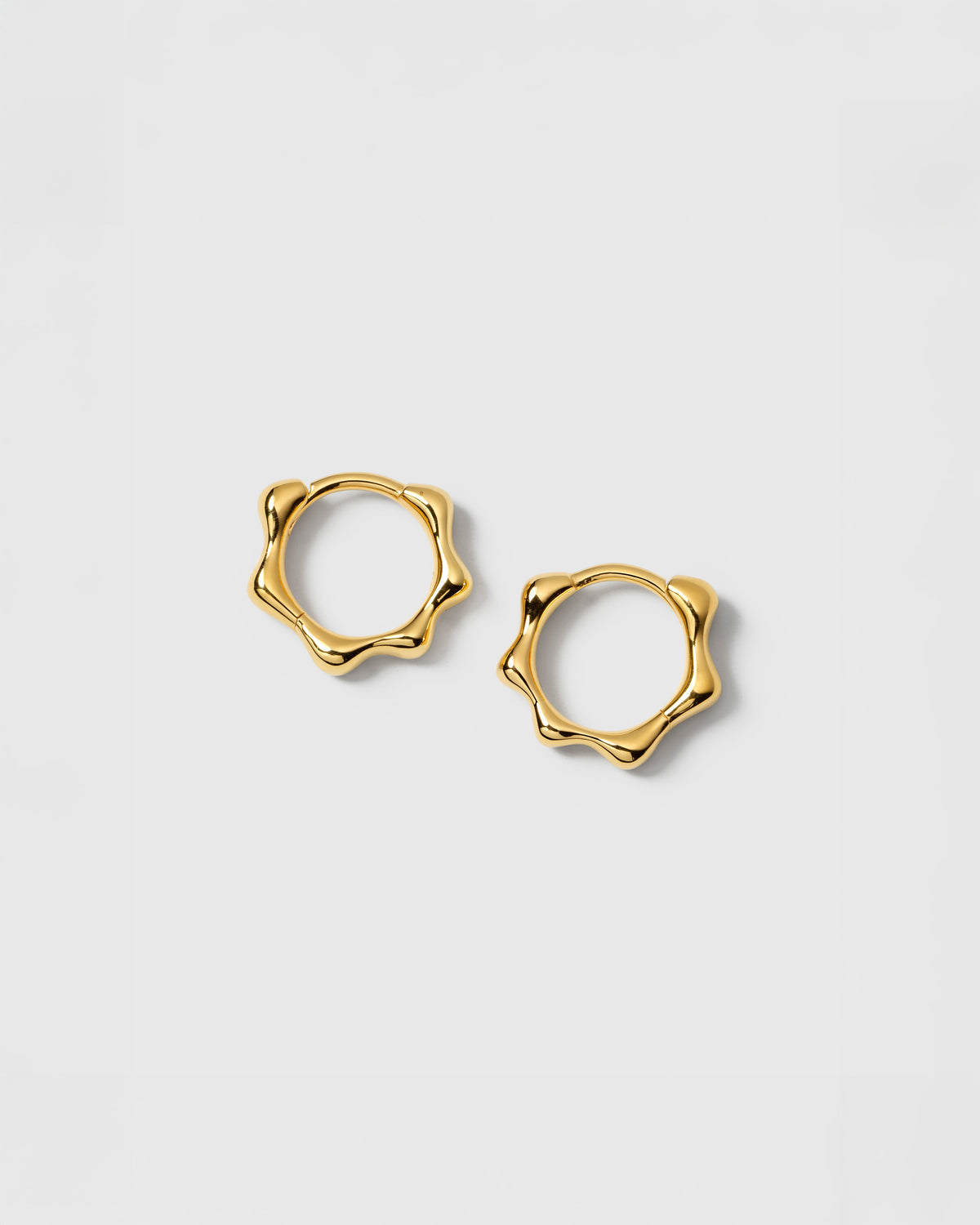 A product shot of the Florentina Small Hoops in gold, showcasing their unique, wavy pattern.