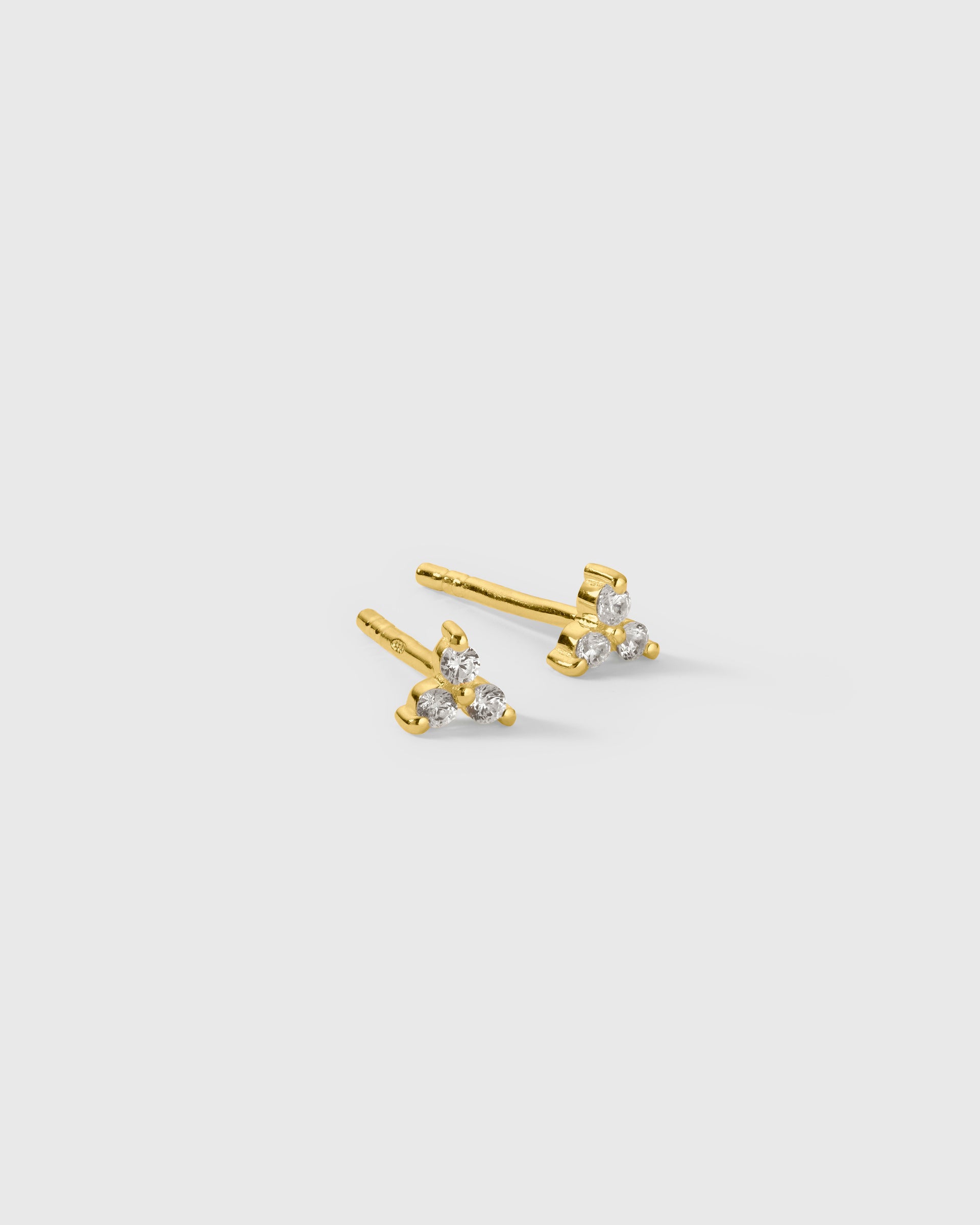A pair of small gold stud earrings each featuring three cubic zirconia stones in a flower-like pattern.