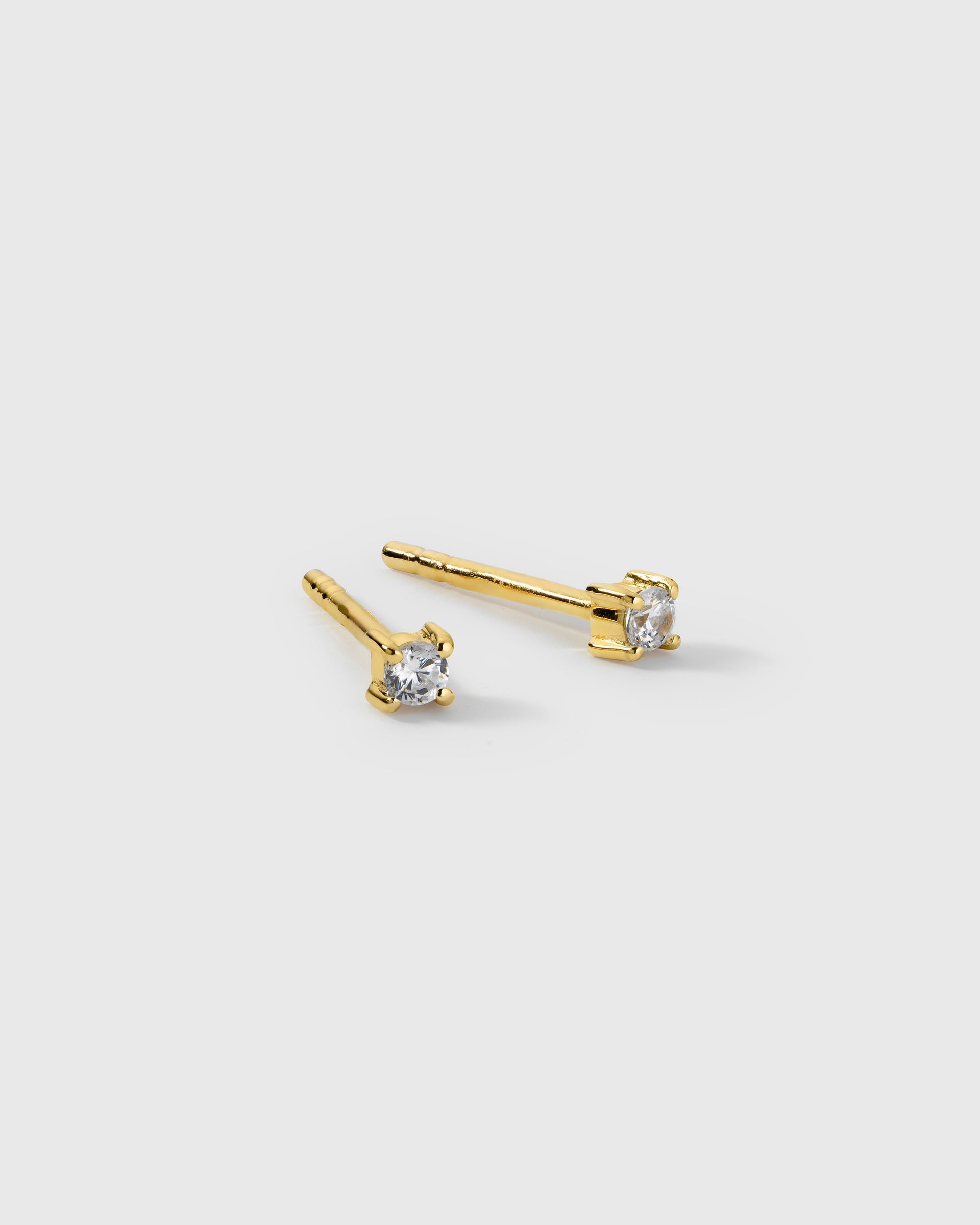 A product shot of the Celestia Mini Studs in gold, featuring a pair of small studs each set with a single cubic zirconia stone.