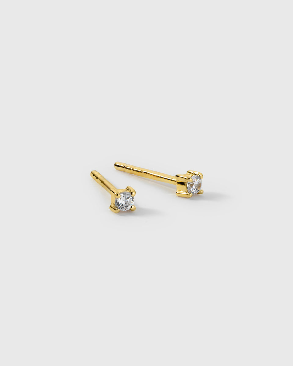 A product shot of the Celestia Mini Studs in gold, featuring a pair of small studs each set with a single cubic zirconia stone.
