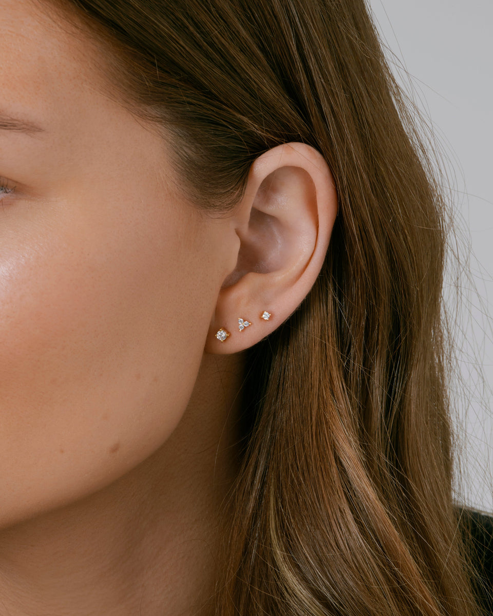 A close-up shot of a model's ear wearing a stack of three gold studs from the Celestia collection, each adorned with cubic zirconia stones.