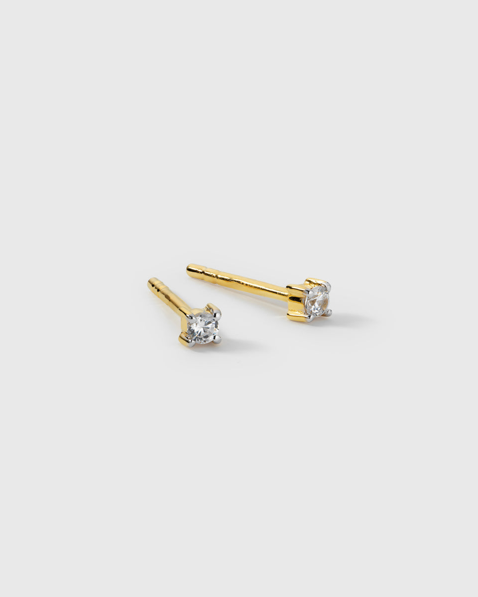 A product shot of the Celestia Mini Studs in gold, featuring a pair of small studs each set with a single cubic zirconia stone.
