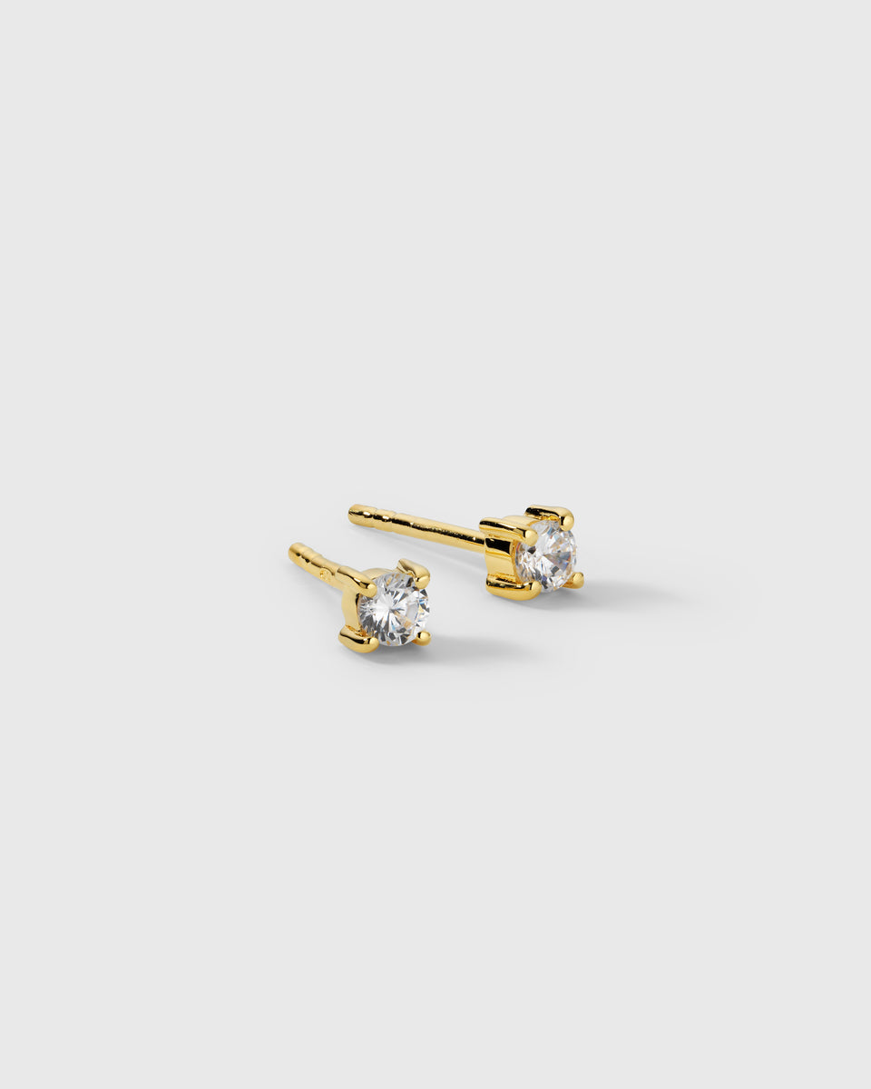 A product shot of the Celestia Small Studs in gold, showcasing the pair of earrings. Each stud features a round cubic zirconia stone held in a classic four-prong setting.