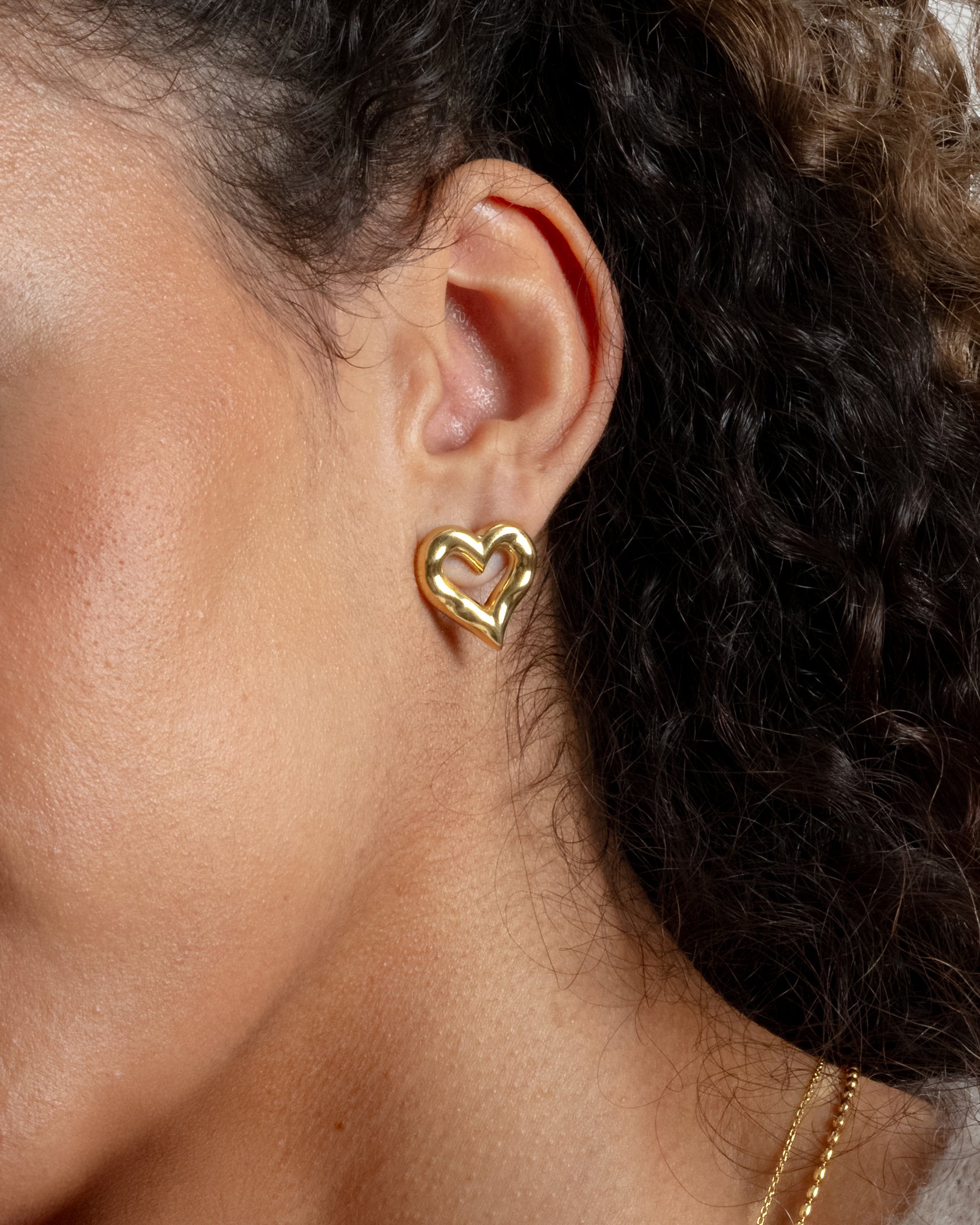 A close-up shot of a model wearing the chunky, gold Puff Heart Earring, showcasing its organic heart shape, with two gold necklace visible.