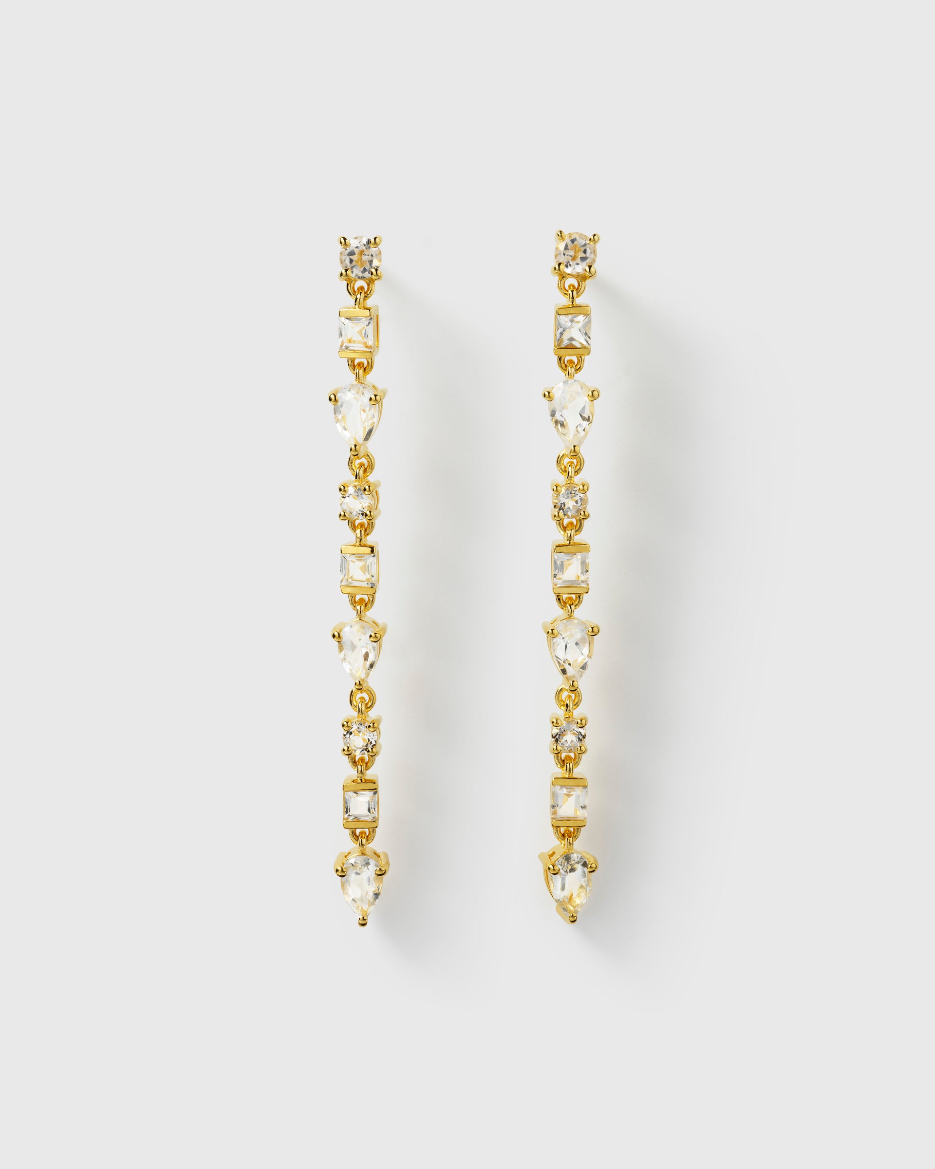 A product shot of the Pam Long Earrings in gold, highlighting their long, elegant design featuring a cascading pattern of white topazes in various shapes.