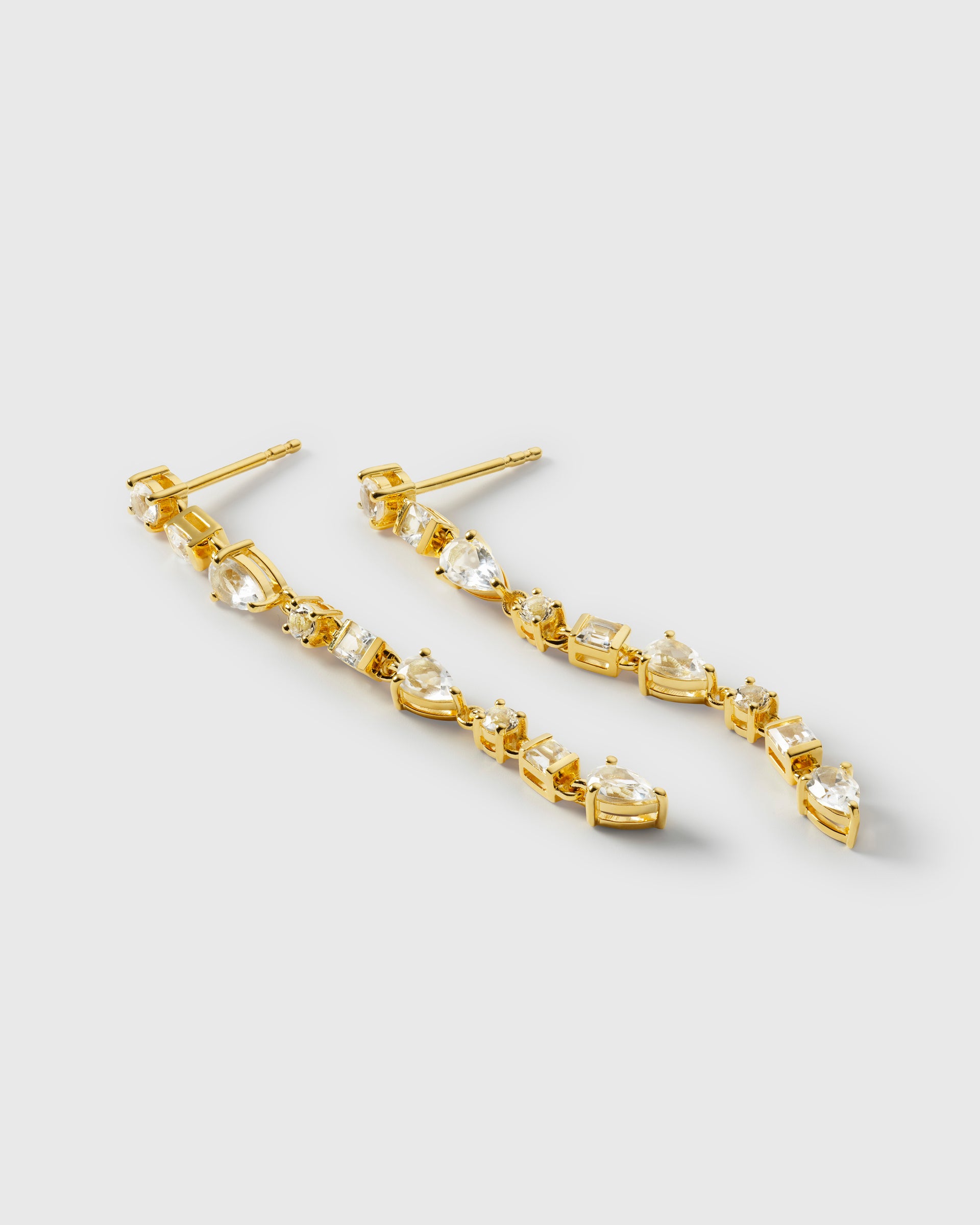 A product shot of the Pam Long Earrings in gold, displaying their elegant, dangling design composed of a sparkling line of multi-shaped white topaz stones.
