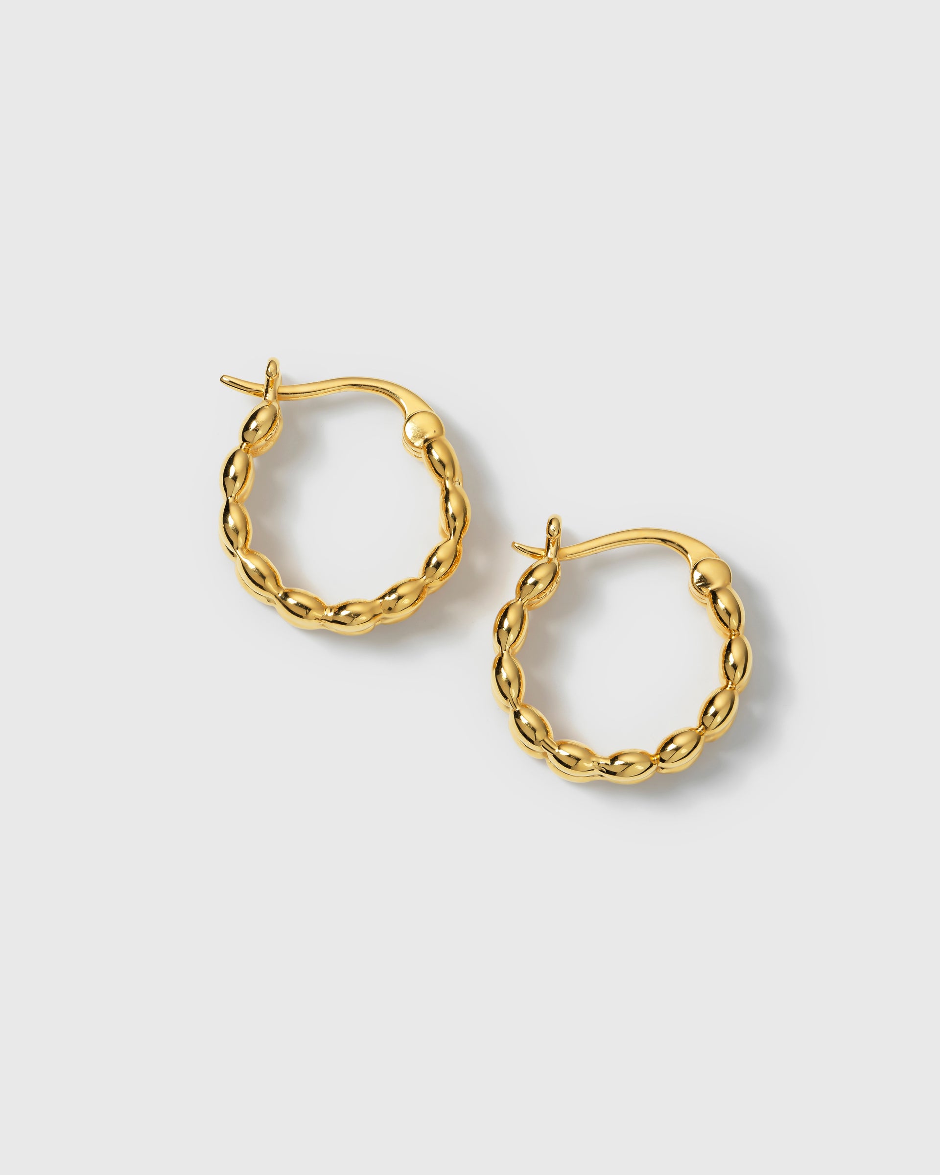 A product shot of the Lunetta Earrings in gold, featuring their unique hoop design composed of a pattern of small ovals.