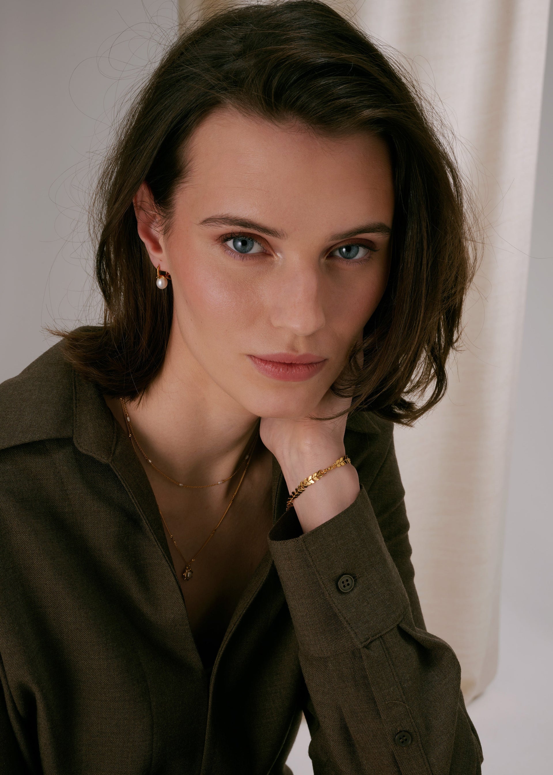 Gold pearl earrings, leaf-design gold bracelet, and layered fine gold necklaces.