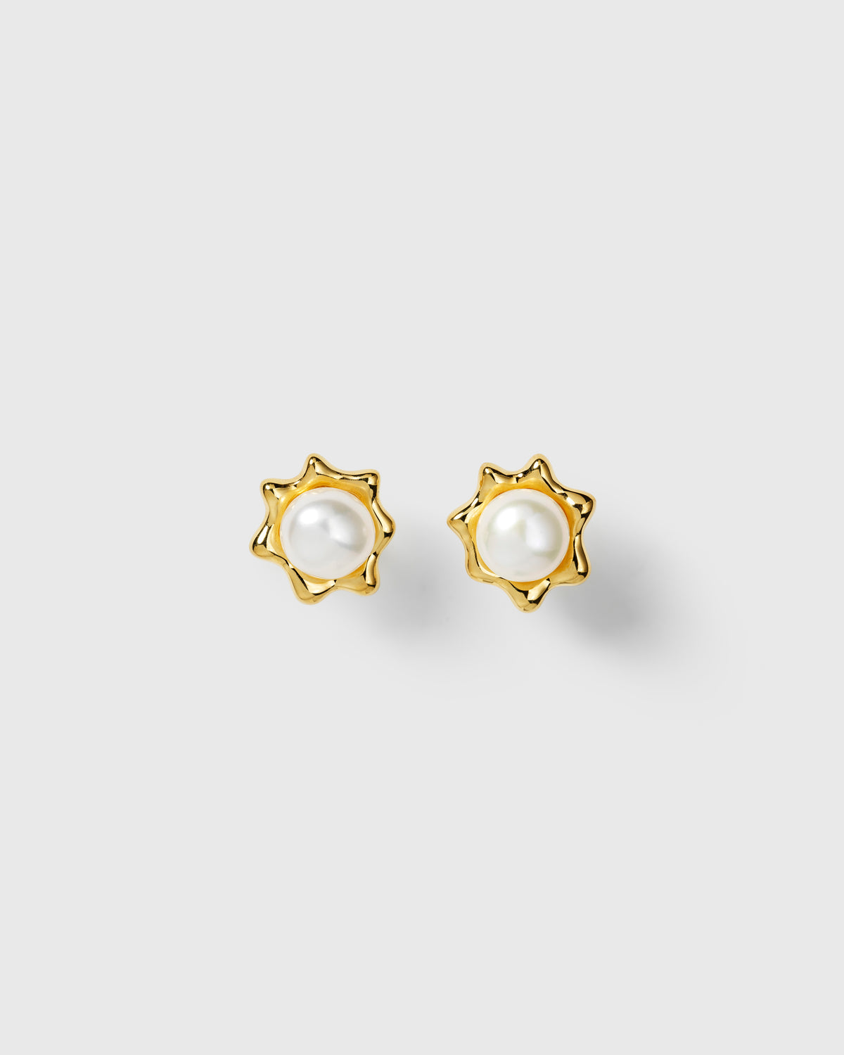 Gold pearl stud earrings with central white pearl in wavy sun-shaped design. 