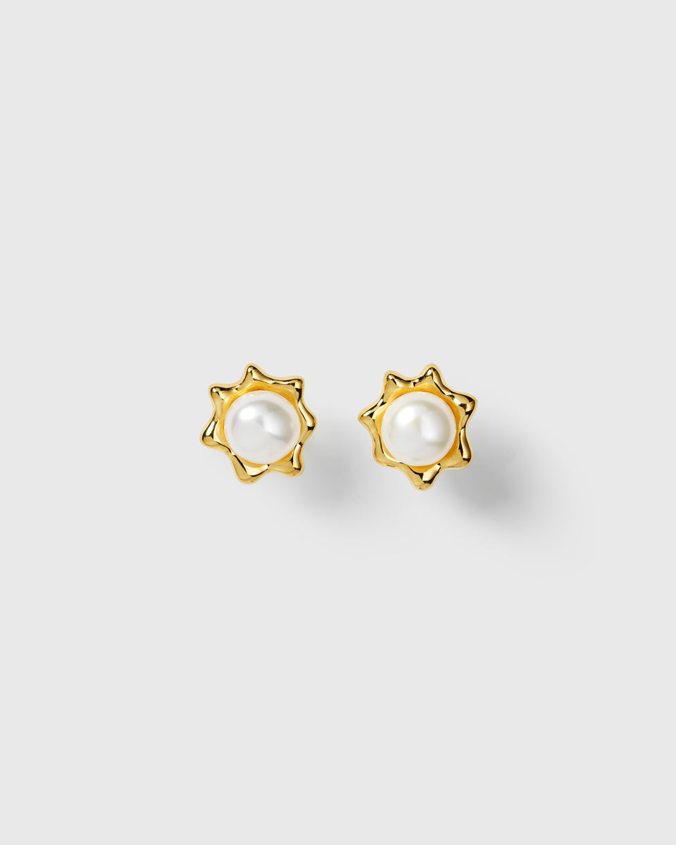 Gold pearl stud earrings with central white pearl in wavy sun-shaped design. 