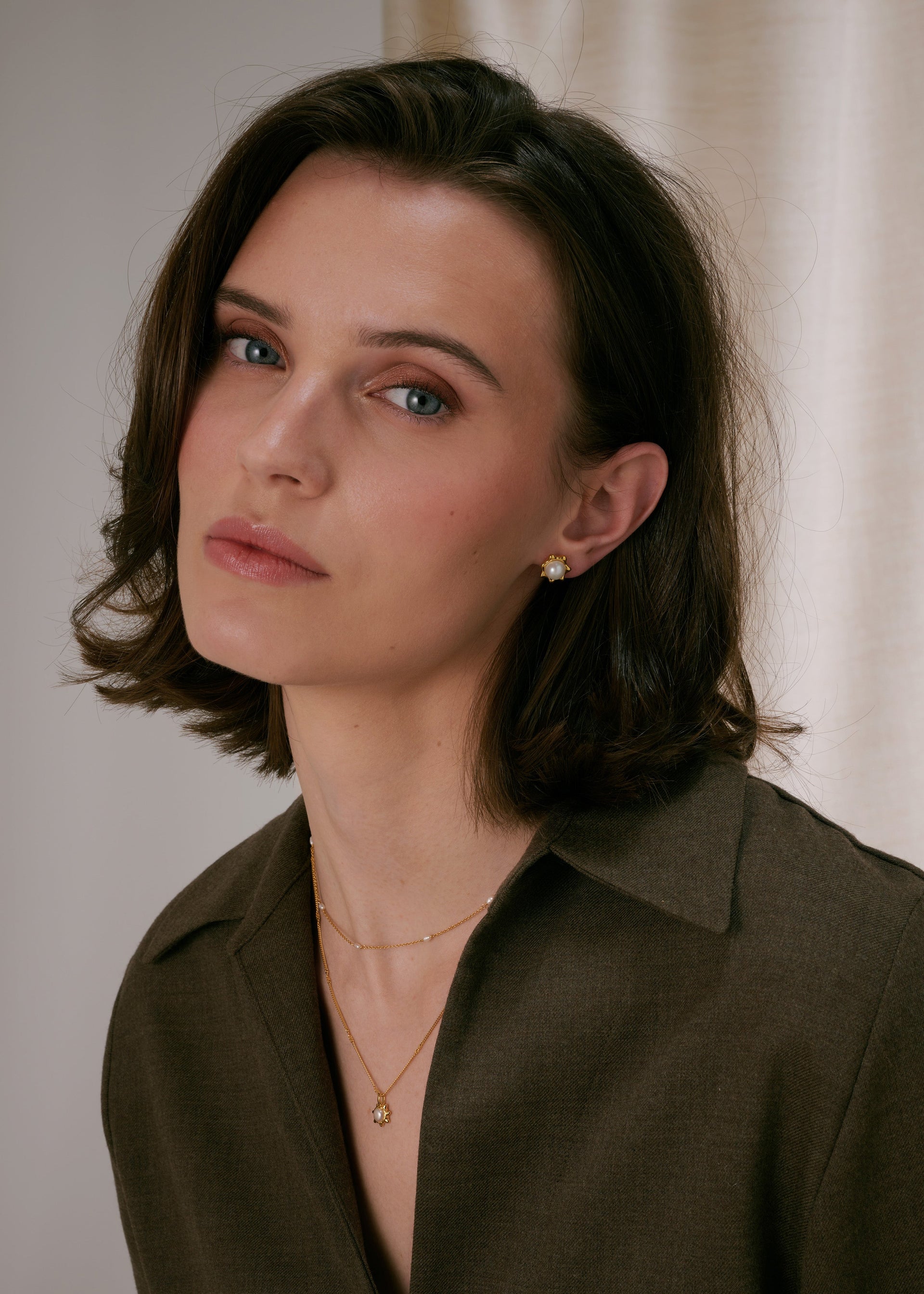 Gold stud earrings with a central freshwater pearl in a floral design, paired with a layered gold necklace—one chain with a matching freshwater pearl pendant and a shorter delicate chain with freshwater pearls.