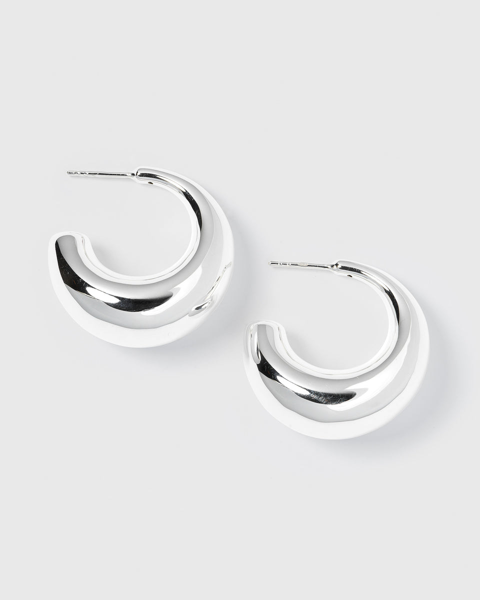 A product shot of the Bolded Earrings in silver, laid out to showcase their unique, chunky and sculptural hoop design.