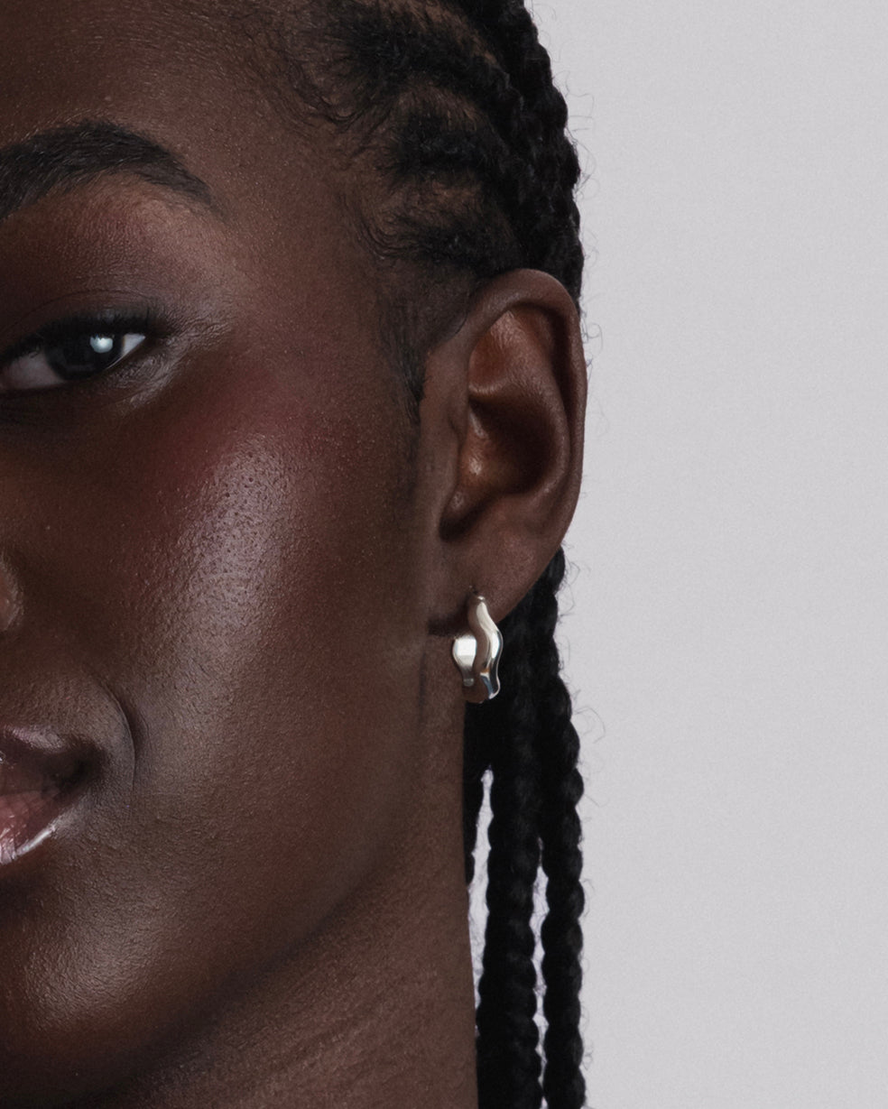 A close-up shot of a model wearing the Bolded Wavy Earrings in silver, highlighting their shiny finish and unique wavy design.