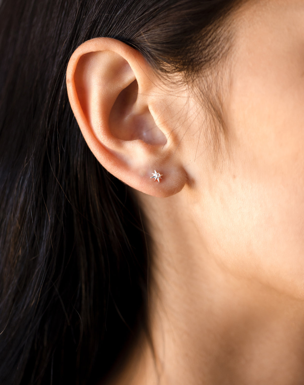 A close-up shot of a model wearing the North Star Stud earring in silver, featuring a delicate star shape with a sparkling crystal at its center.