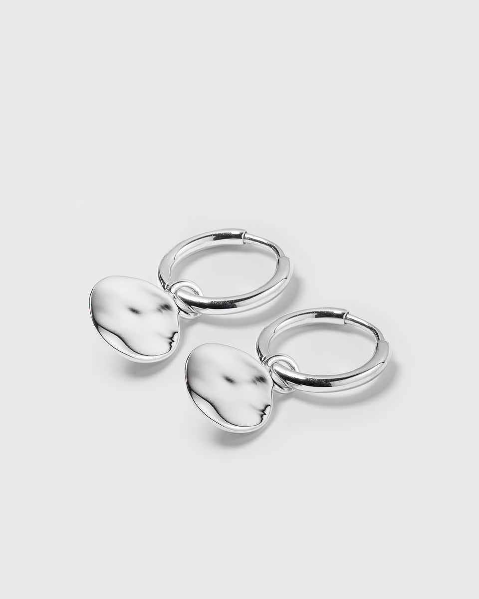 A product shot of the Minimalistica Hammered Earrings in silver, featuring small hoops with dangling pendants that have a hammered surface.