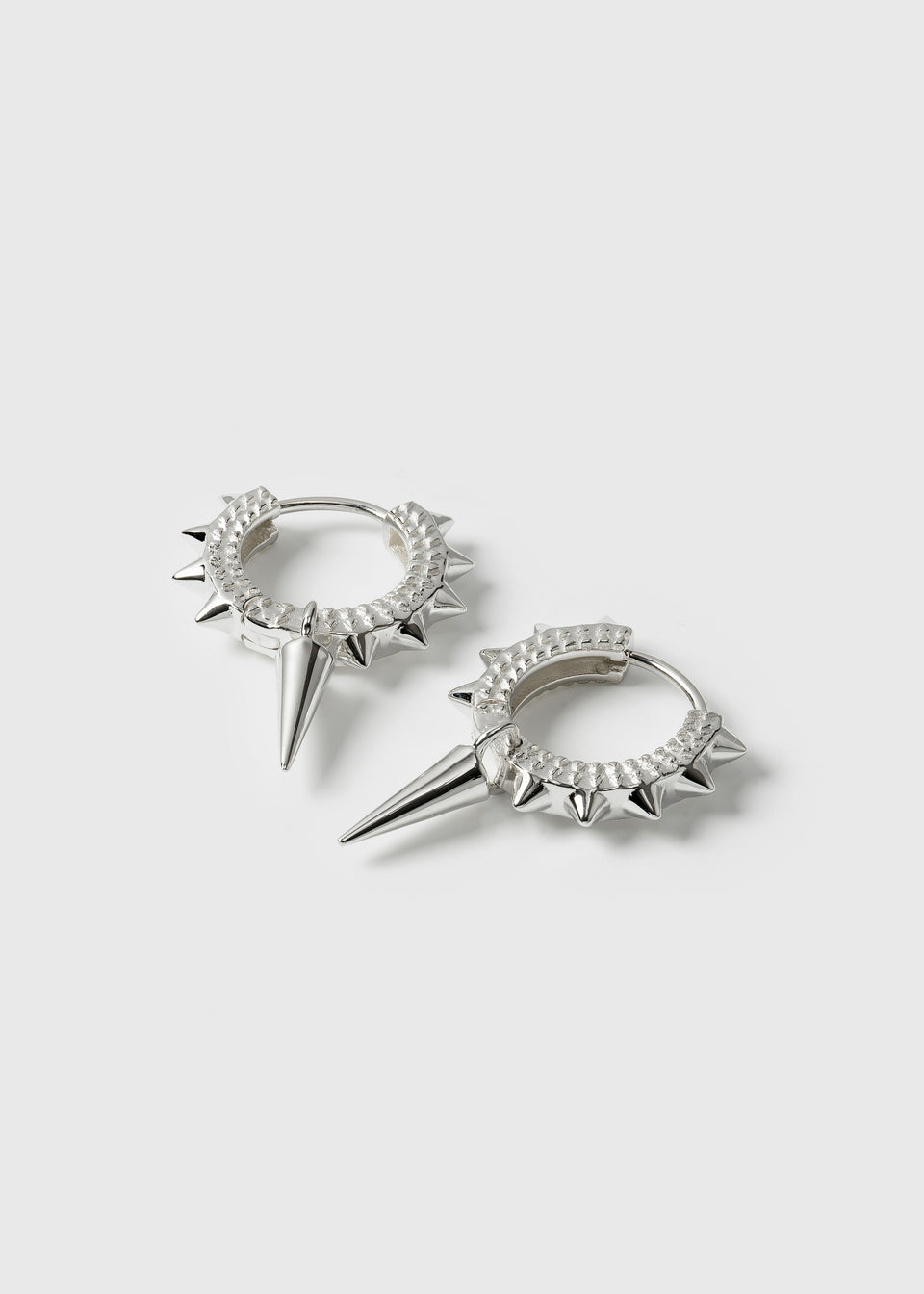A product shot of the Harvey Heavy Spike Hoops in silver, featuring textured hoops with small spikes and a larger, dangling spike pendant.