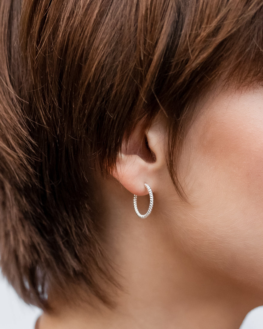 A close-up shot of a model wearing the Beloved Twisted Medium Hoops in silver, highlighting their detailed twisted pattern.