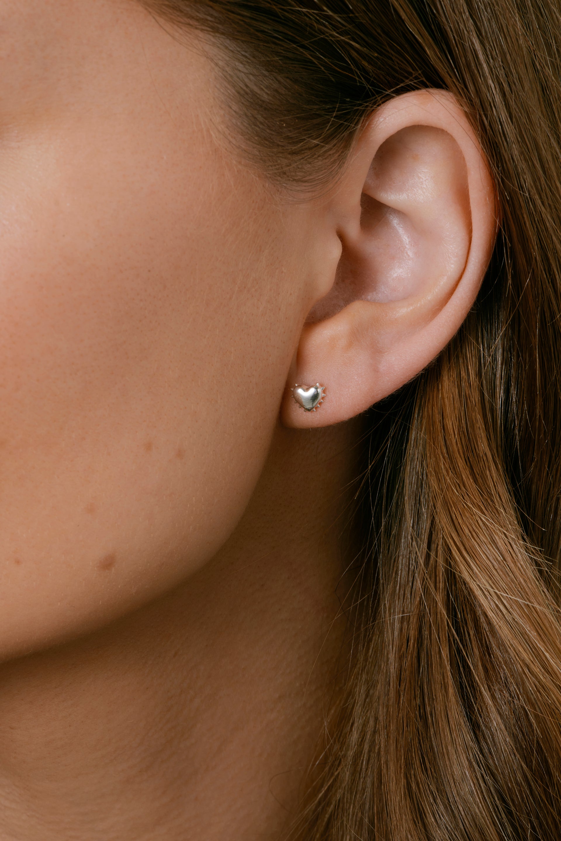 A close-up of a model wearing the silver True Love Spike Heart Stud, an earring designed as a heart with small, edgy spikes.