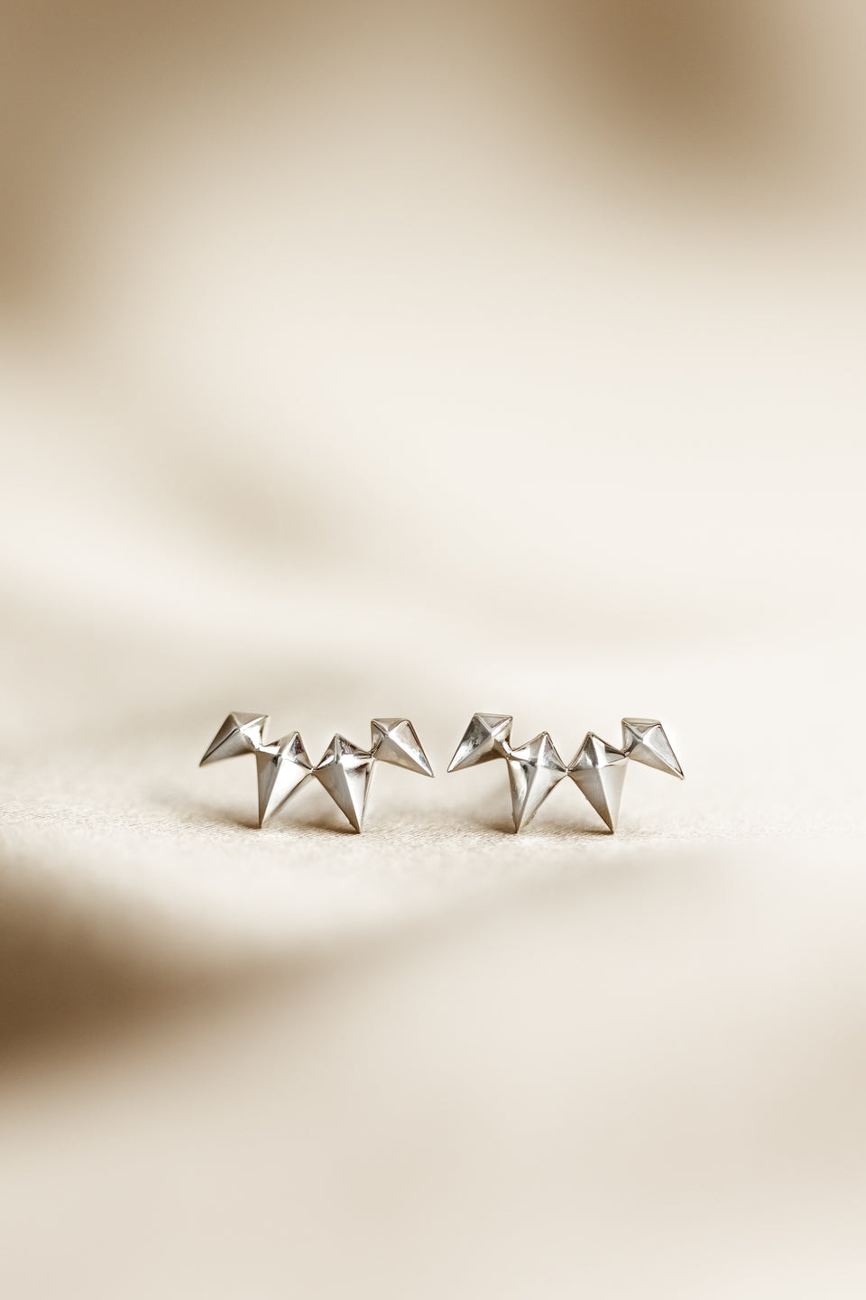 A product shot of the Uma Climber Earrings in silver, laid out to display their design of a row of small, polished spikes.