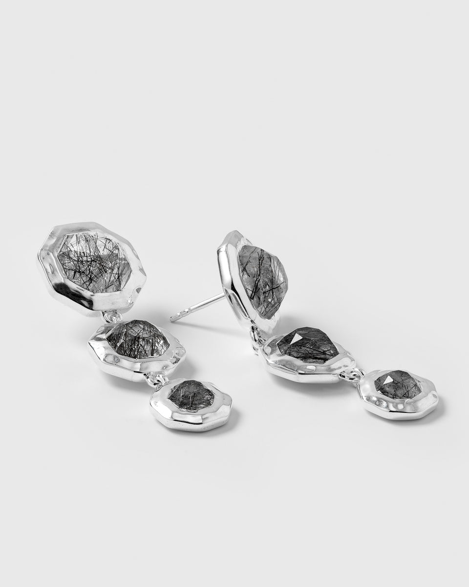 A product shot of the Octagon Earrings in silver, a pair of long, dangling earrings each set with three octagon-shaped black rutile quartz stones.