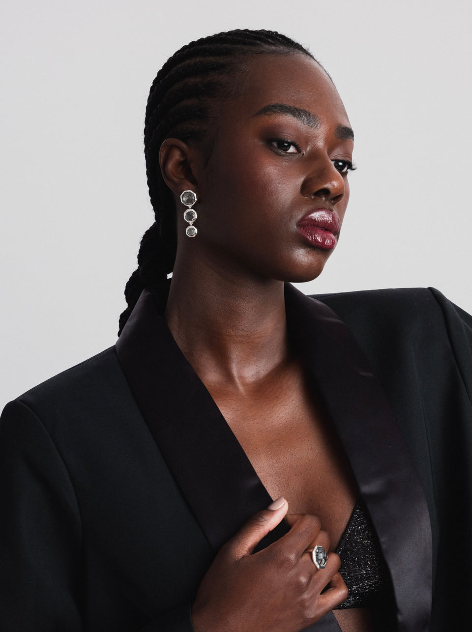 A close-up of a model wearing the silver Octagon Earrings, featuring three dangling octagon-shaped black rutile quartz stones, and the matching Octagon ring.