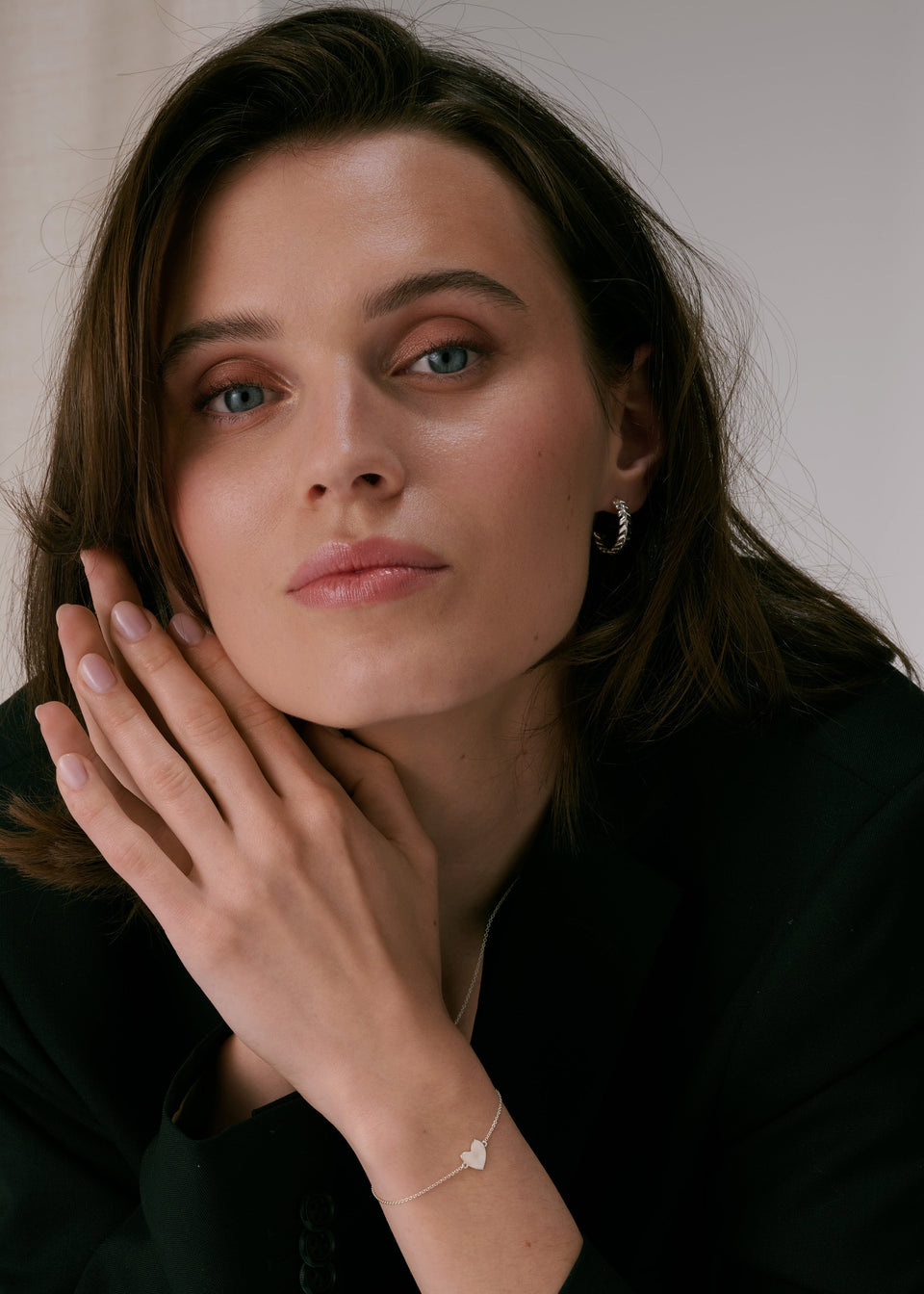 Silver hoop earrings with a leaf-like pattern, paired with a delicate silver chain bracelet featuring a heart charm.