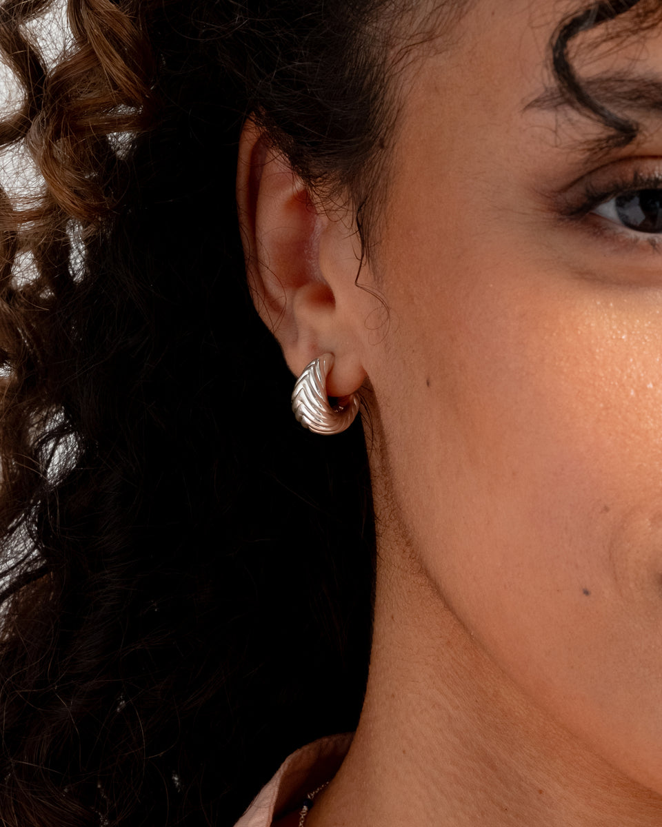 A close-up shot of a model wearing the Bolded Little Sis Chevron Earrings in silver, highlighting their chunky design and distinctive chevron pattern.