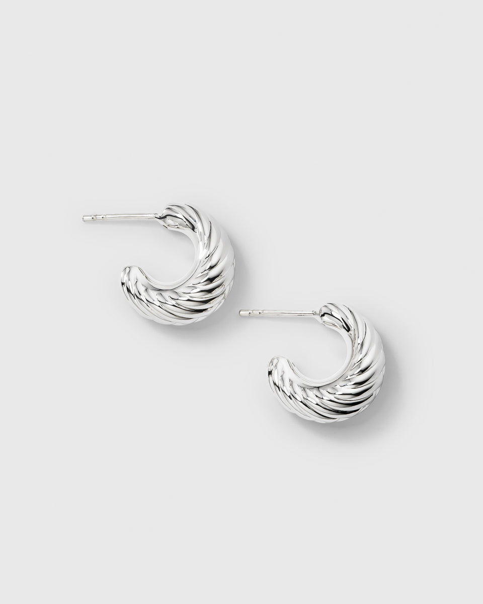 A product shot of the Bolded Little Sis Chevron Earrings in silver, laid out to display their chunky C-hoop shape and textured chevron pattern.