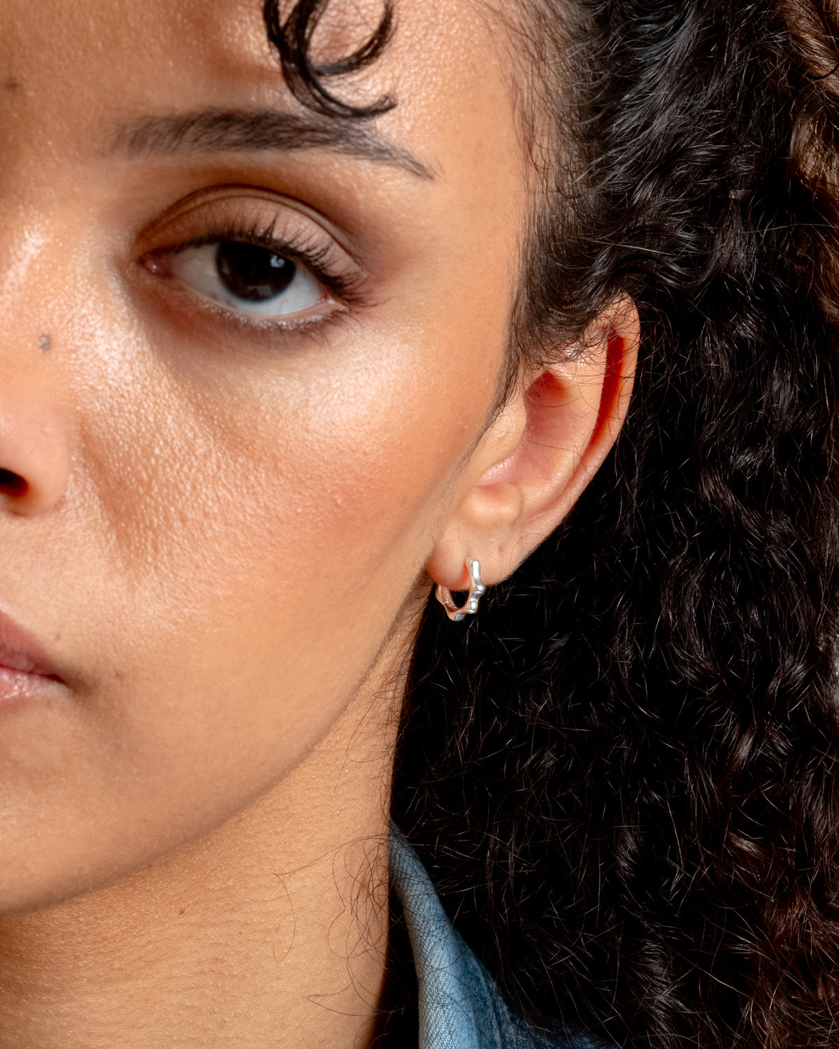 A close-up shot of a model wearing the Florentina Small Hoops in silver, highlighting their unique wavy design.