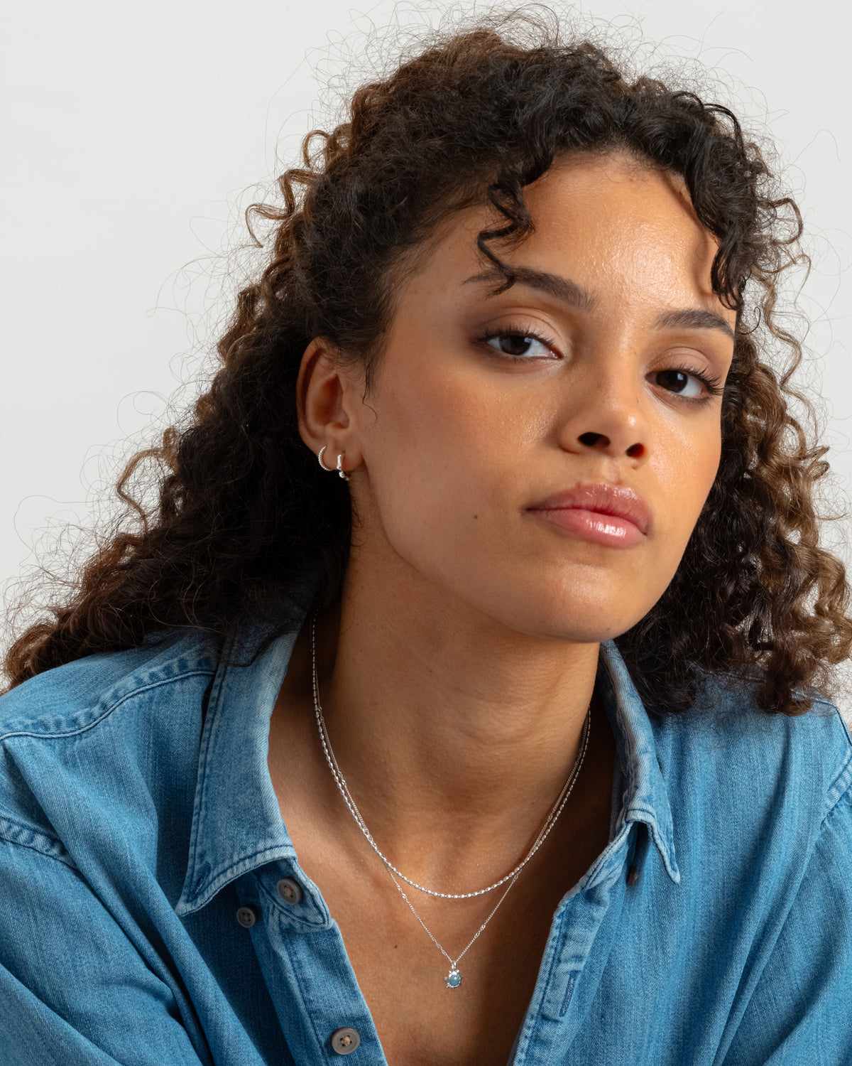 A close-up shot of a model wearing the Florentina Small Hoops in silver, along with another small, simple silver hoop and two layered silver necklaces.
