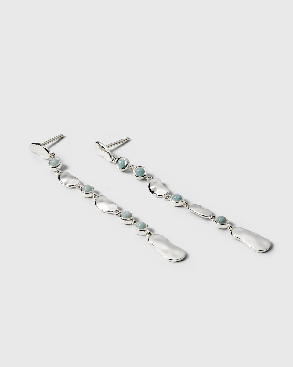 A product shot of the Florentina Long Earrings Silver Aquamarine, displaying their long, dangling design composed of hammered silver plates alternating with round, light blue aquamarine stones.