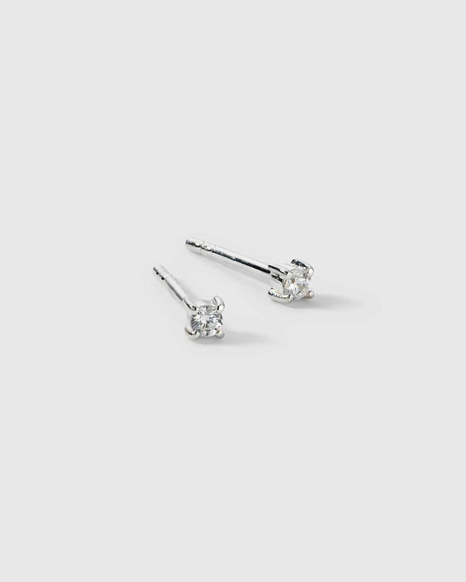 A product shot of the Celestia Mini Studs in silver, a pair of small stud earrings each featuring a round cubic zirconia stone held in a four-prong setting.