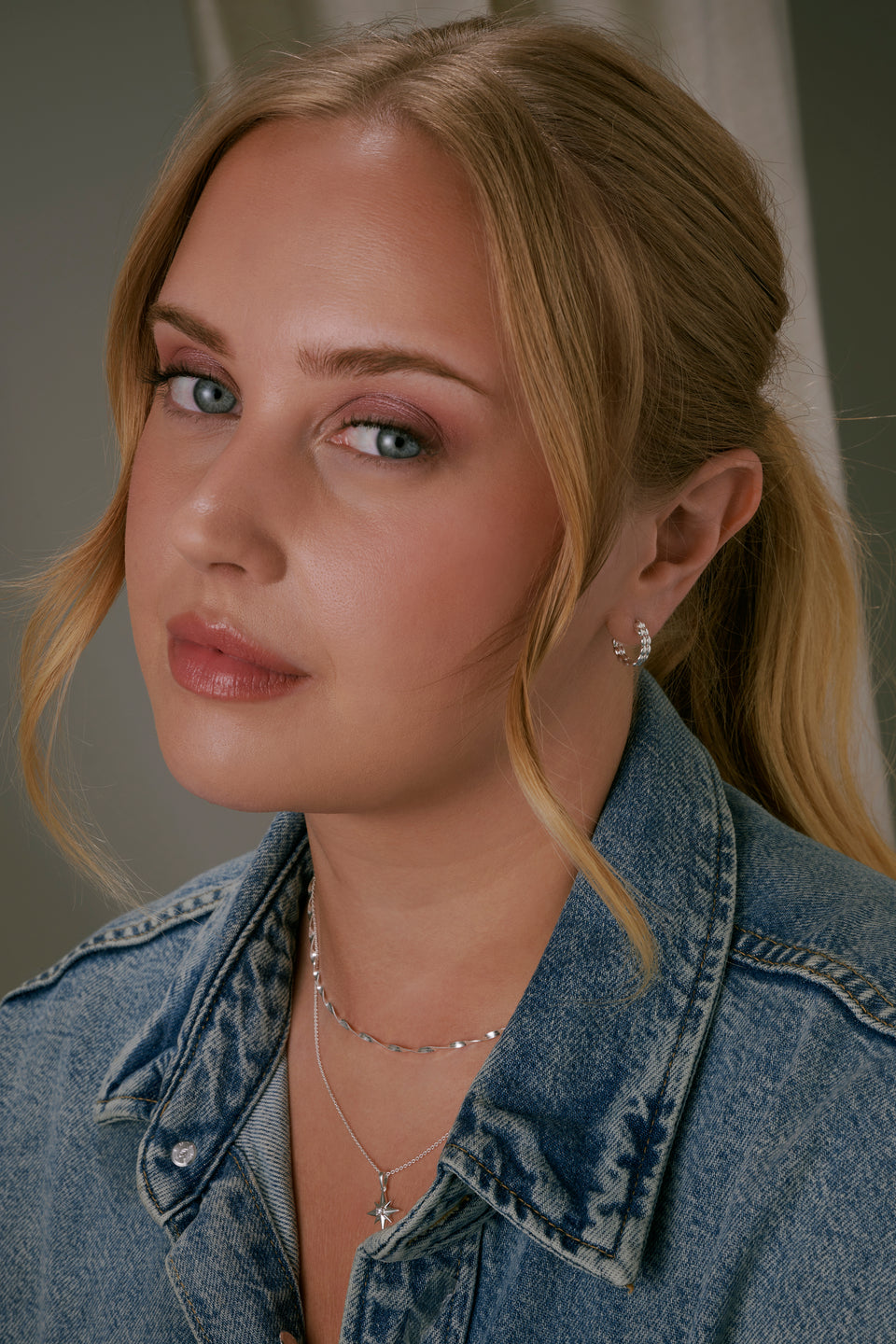 A shot of a model wearing the Lunetta Earrings in silver, showcasing their unique design of two parallel hoops joined by a pattern of small ovals.