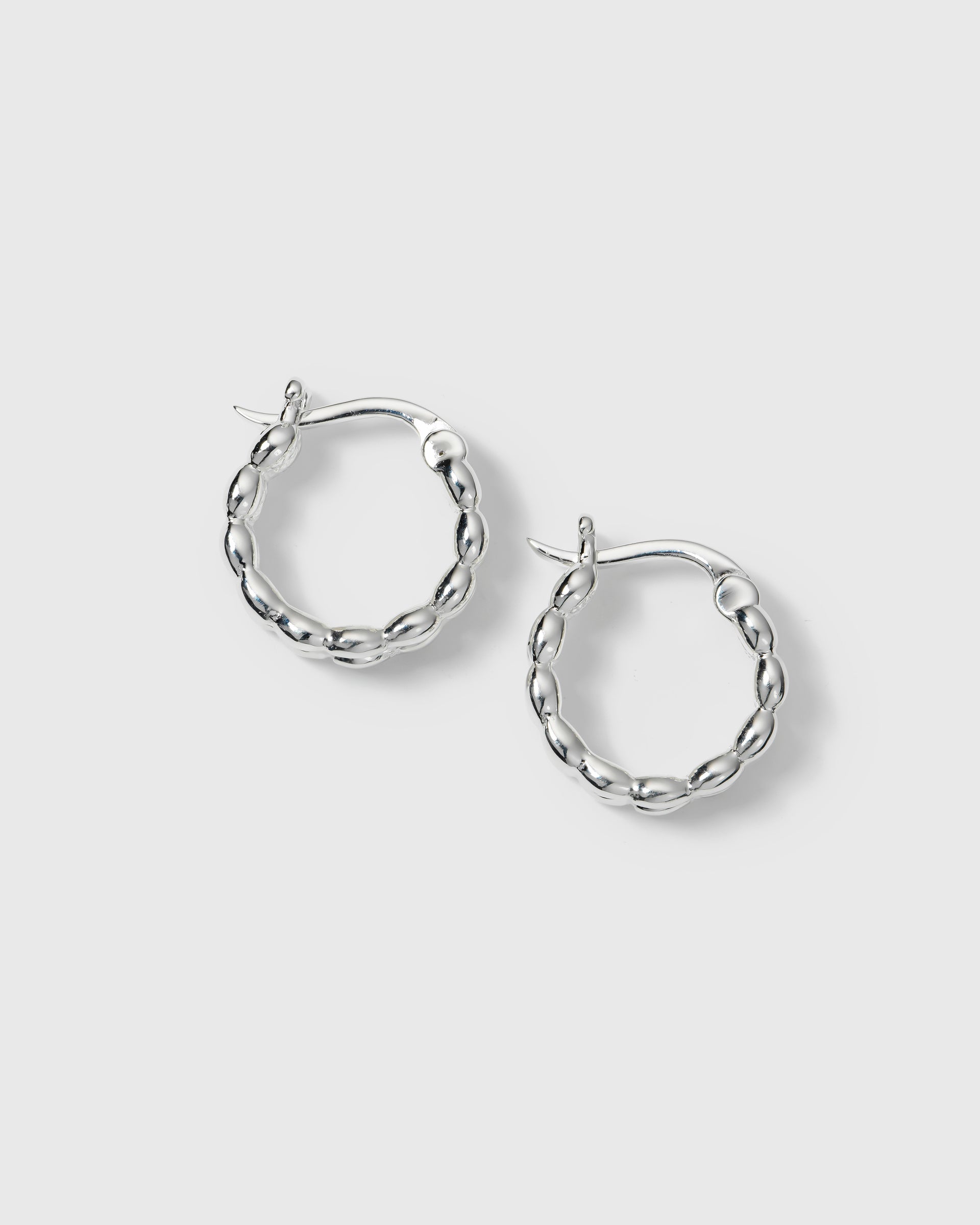 A product shot of the silver Lunetta Earrings, showcasing their unique hoop design formed by a pattern of small ovals.