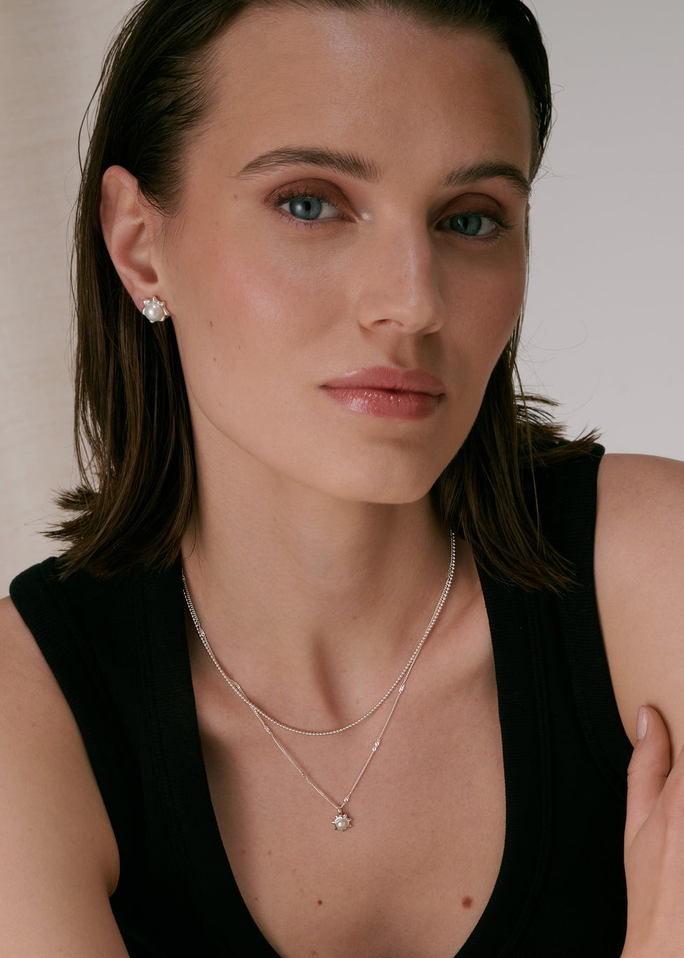 Silver stud earrings with freshwater pearls in a floral setting, paired with a layered silver necklace featuring a matching pearl pendant.