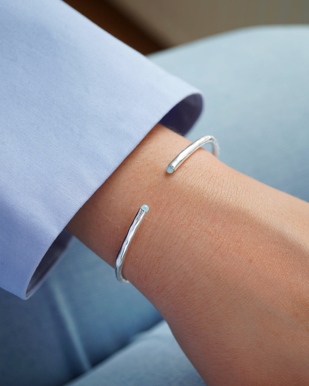 A close-up shot of a model wearing the Florentina Bangle in silver, showing its hammered texture and the light blue aquamarine stones at each end of the cuff.