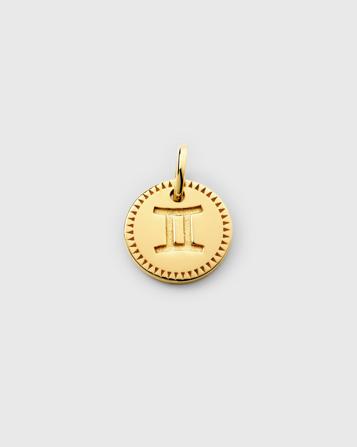 A product shot of the Beloved Zodie Pendant in gold, showcasing the Gemini variant with its zodiac symbol engraved in the center of the circular charm, framed by a decorative triangular pattern.