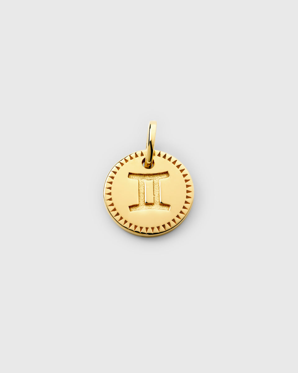 A product shot of the Beloved Zodie Pendant in gold, showcasing the Gemini variant with its zodiac symbol engraved in the center of the circular charm, framed by a decorative triangular pattern.