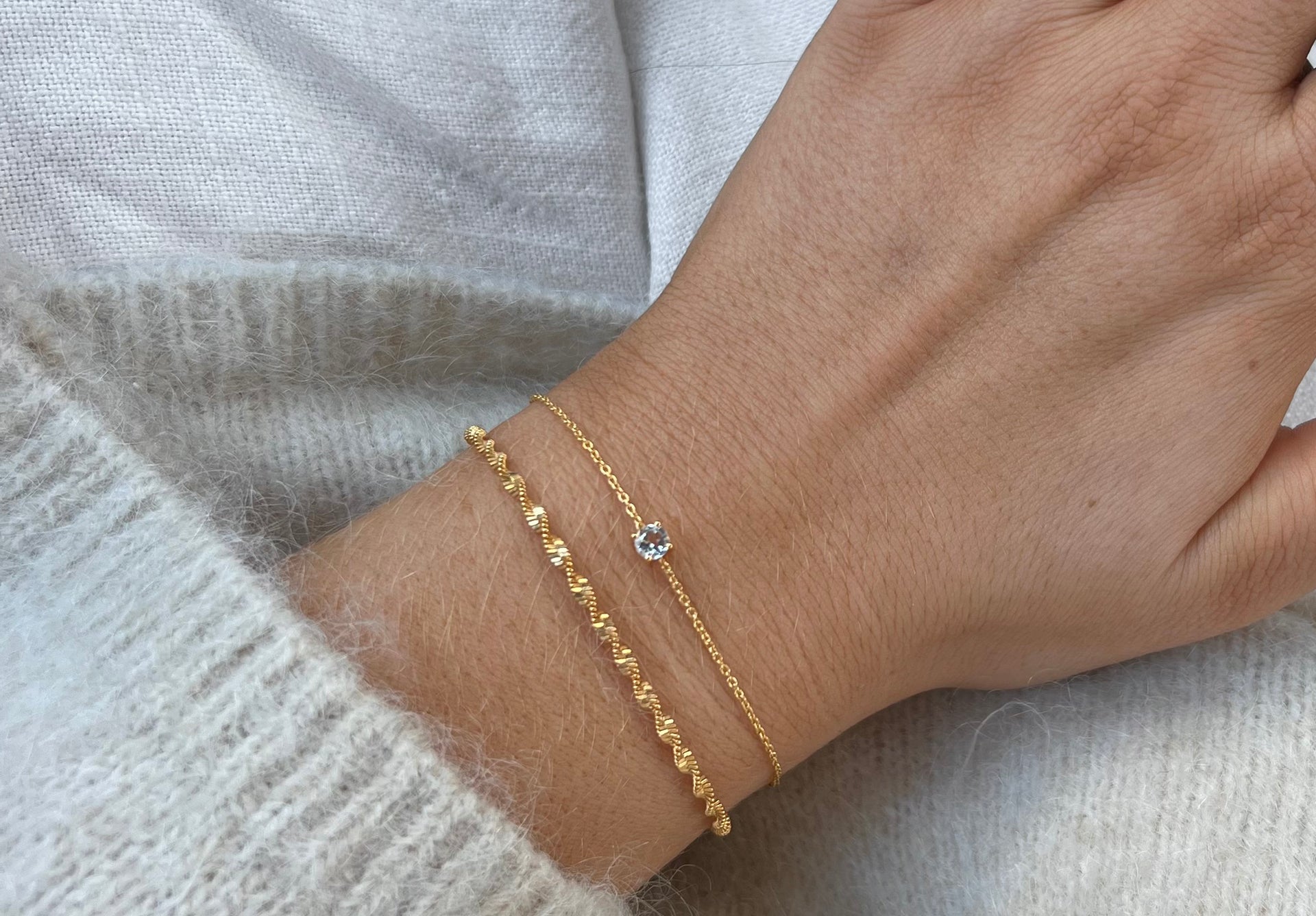 Two bracelets in gold, one with a sparkling stone and one with a twisted look.