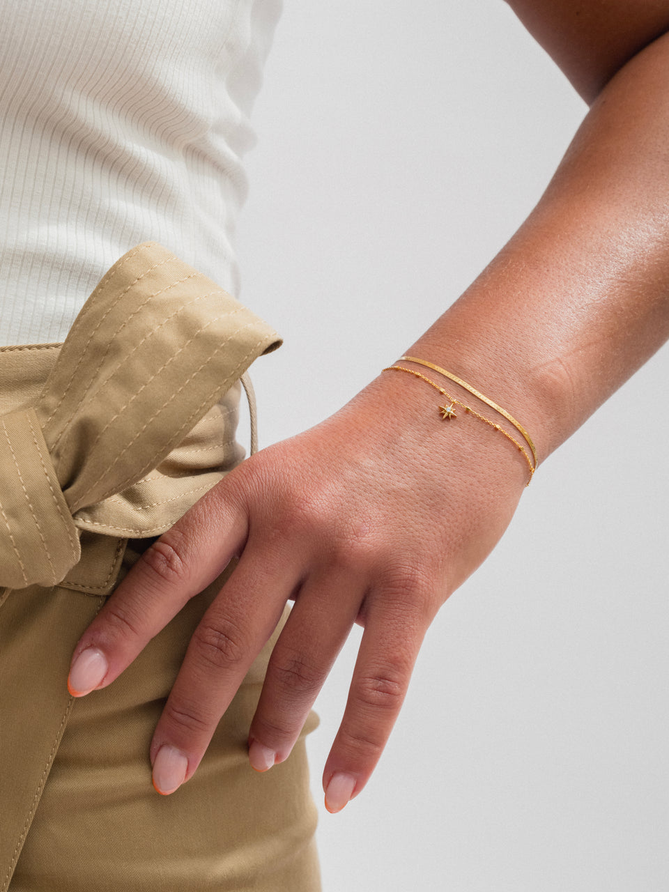 A model's wrist adorned with the gold North Star Bracelet, featuring a delicate chain and a star charm, layered with the sleek gold Herringbone Bracelet.